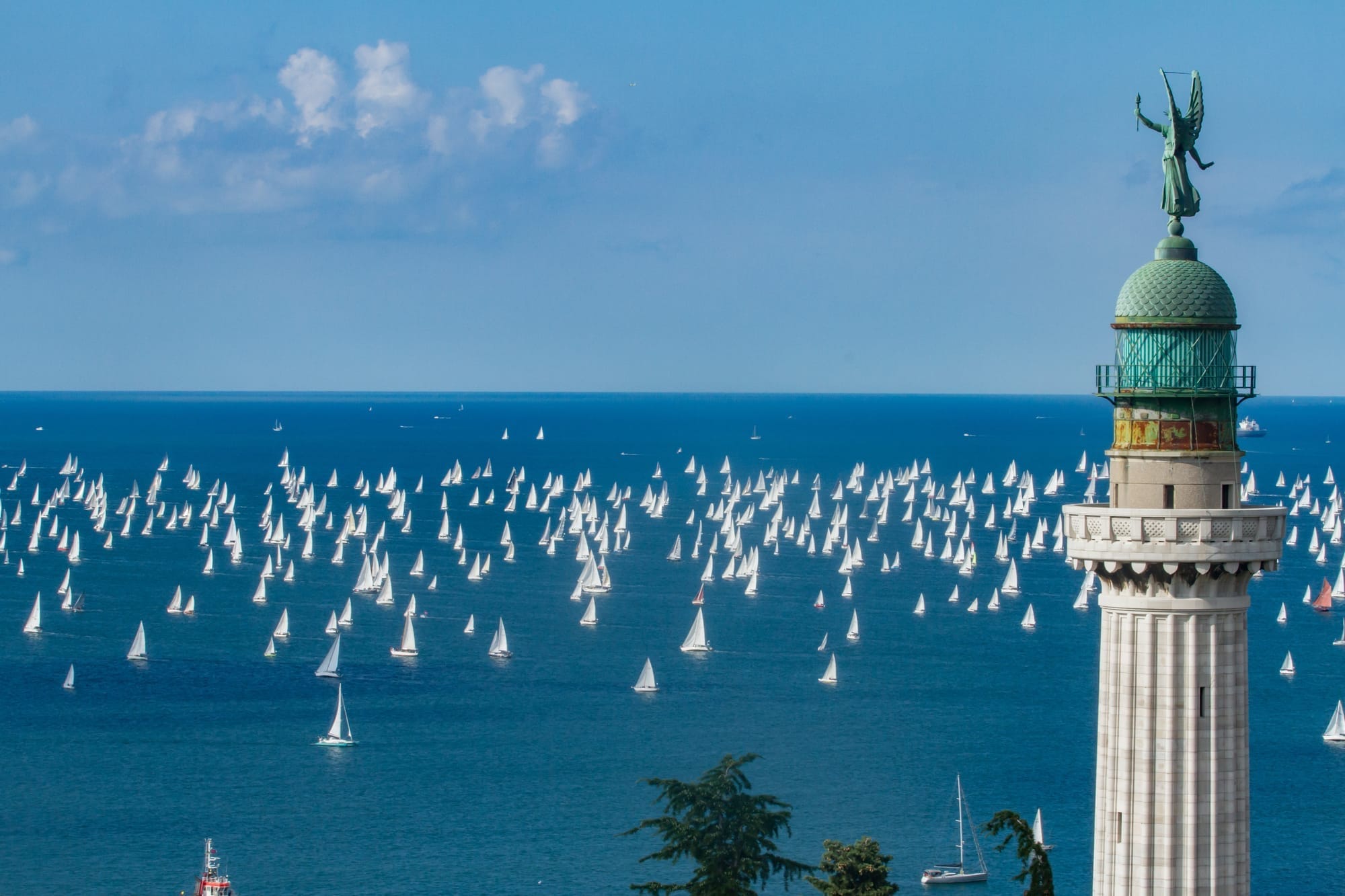A statue in Trieste, Italy, overlooking the Adriatic Sea filled with thousands of sailboats during the annual Barcolana regatta on a sunny October day.