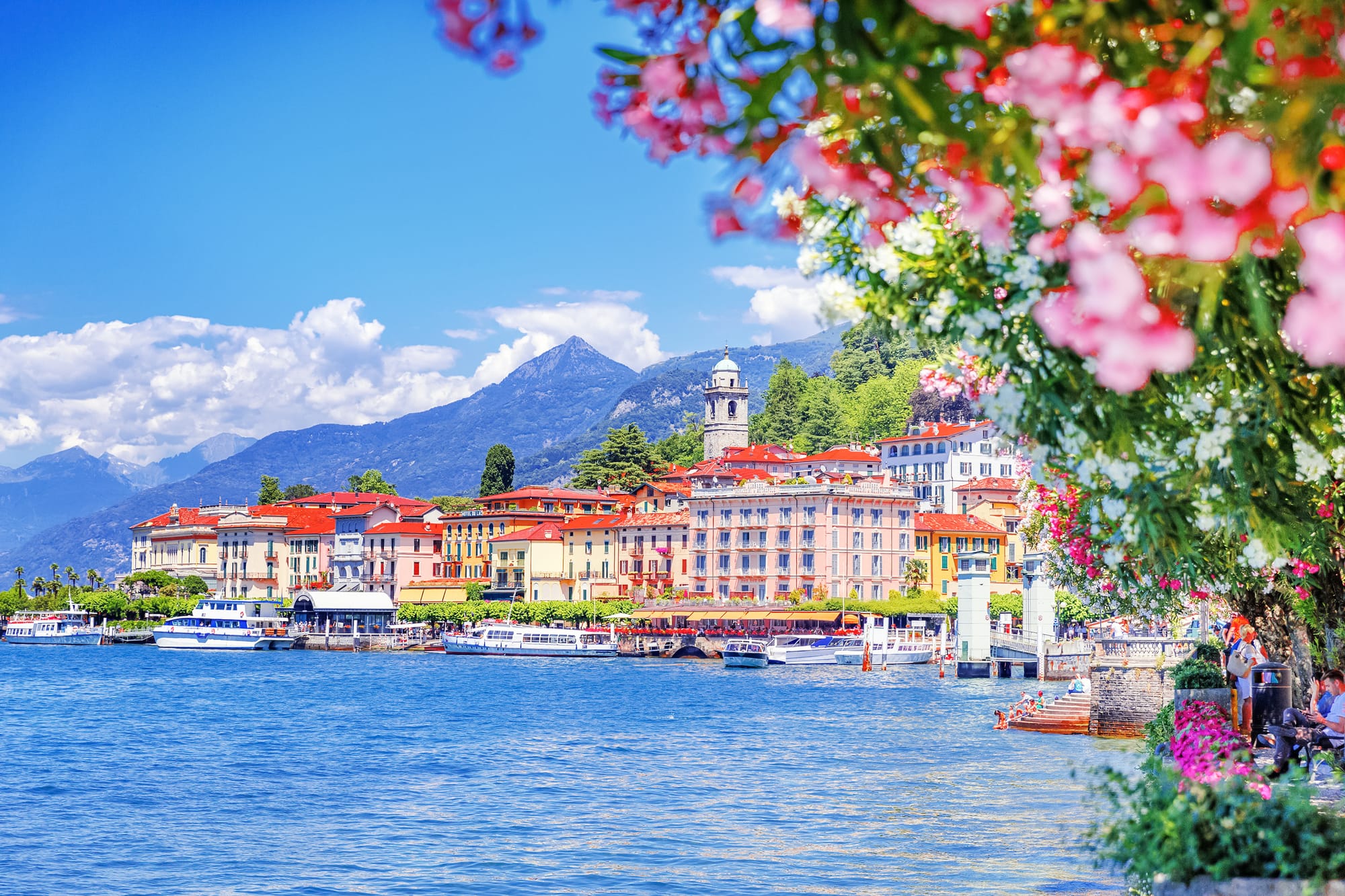 The picturesque town of Bellagio on Lake Como in spring, with colorful buildings and blooming purple flowers framing the water.