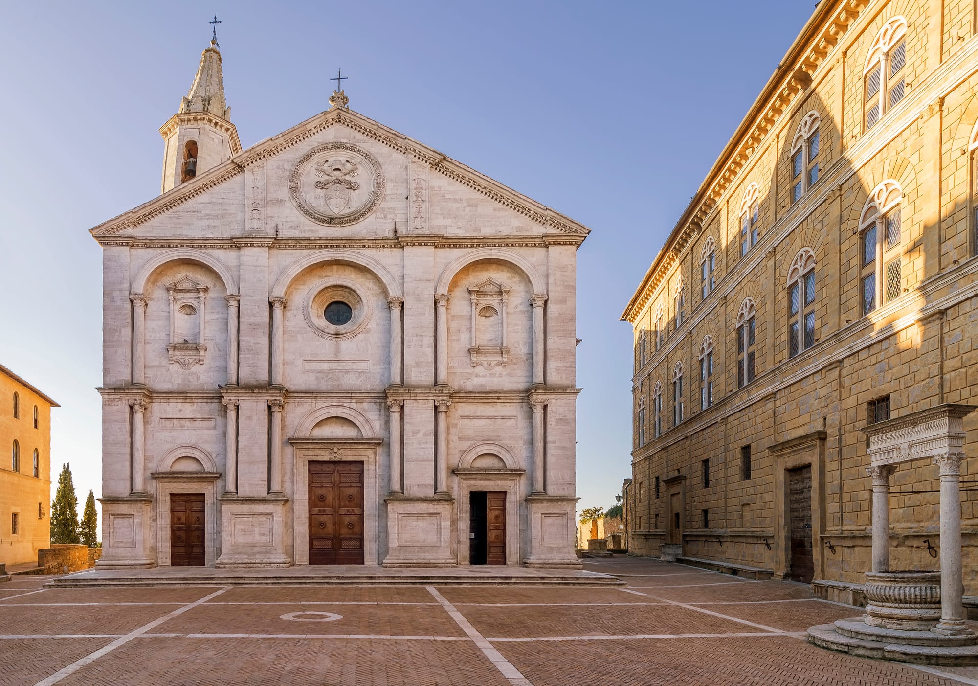 The Renaissance facade of the Duomo in Pienza, Val d'Orcia, illuminated by the warm light of sunrise on Piazza Pio II.