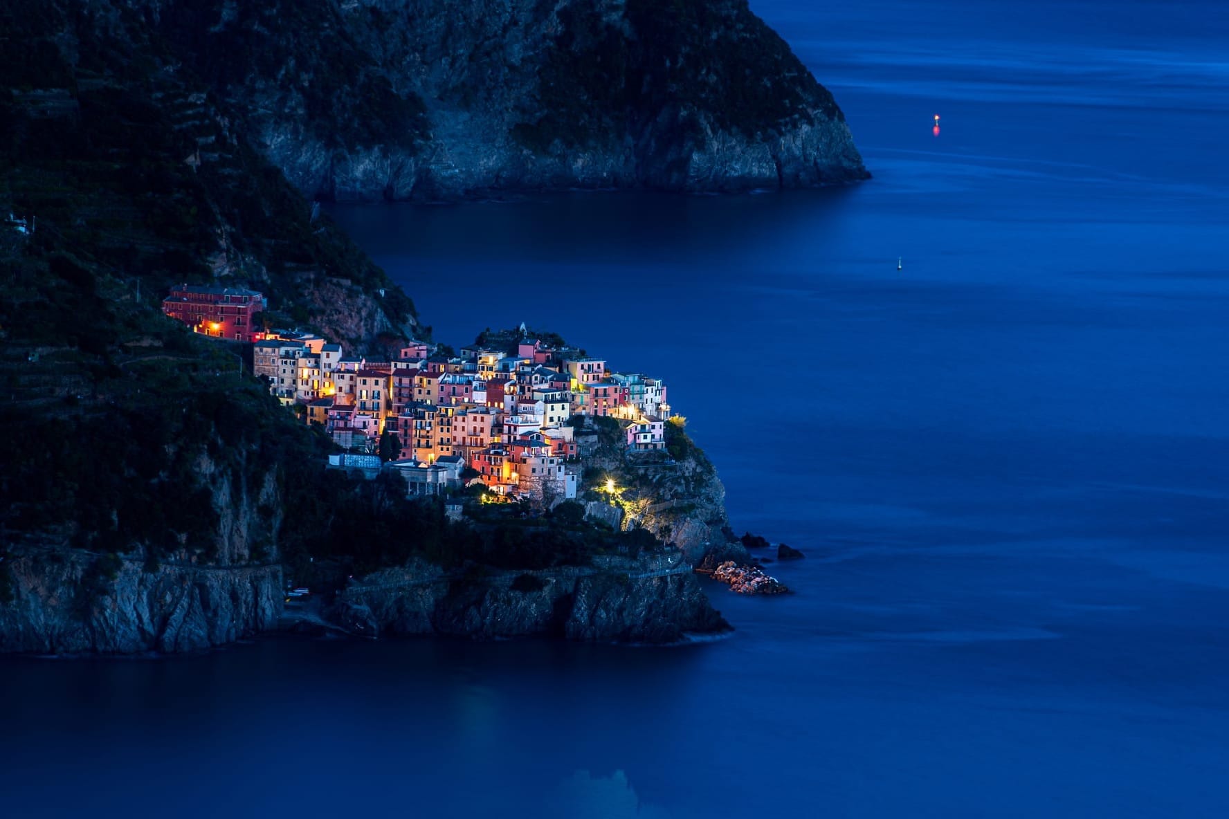 Colorful houses of a typical Italian fishing village, like those in Cinque Terre, clustered around a small harbor during the blue hour after sunset.