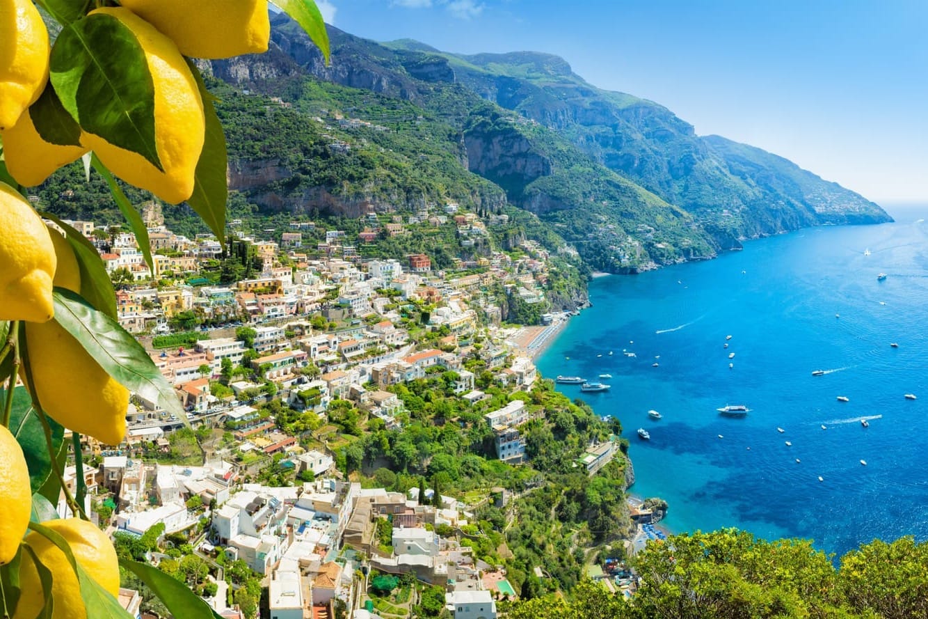 Iconic view of the colorful cliffside houses of Positano on the Amalfi Coast, overlooking the clear blue Mediterranean sea with bright yellow lemons in the foreground.