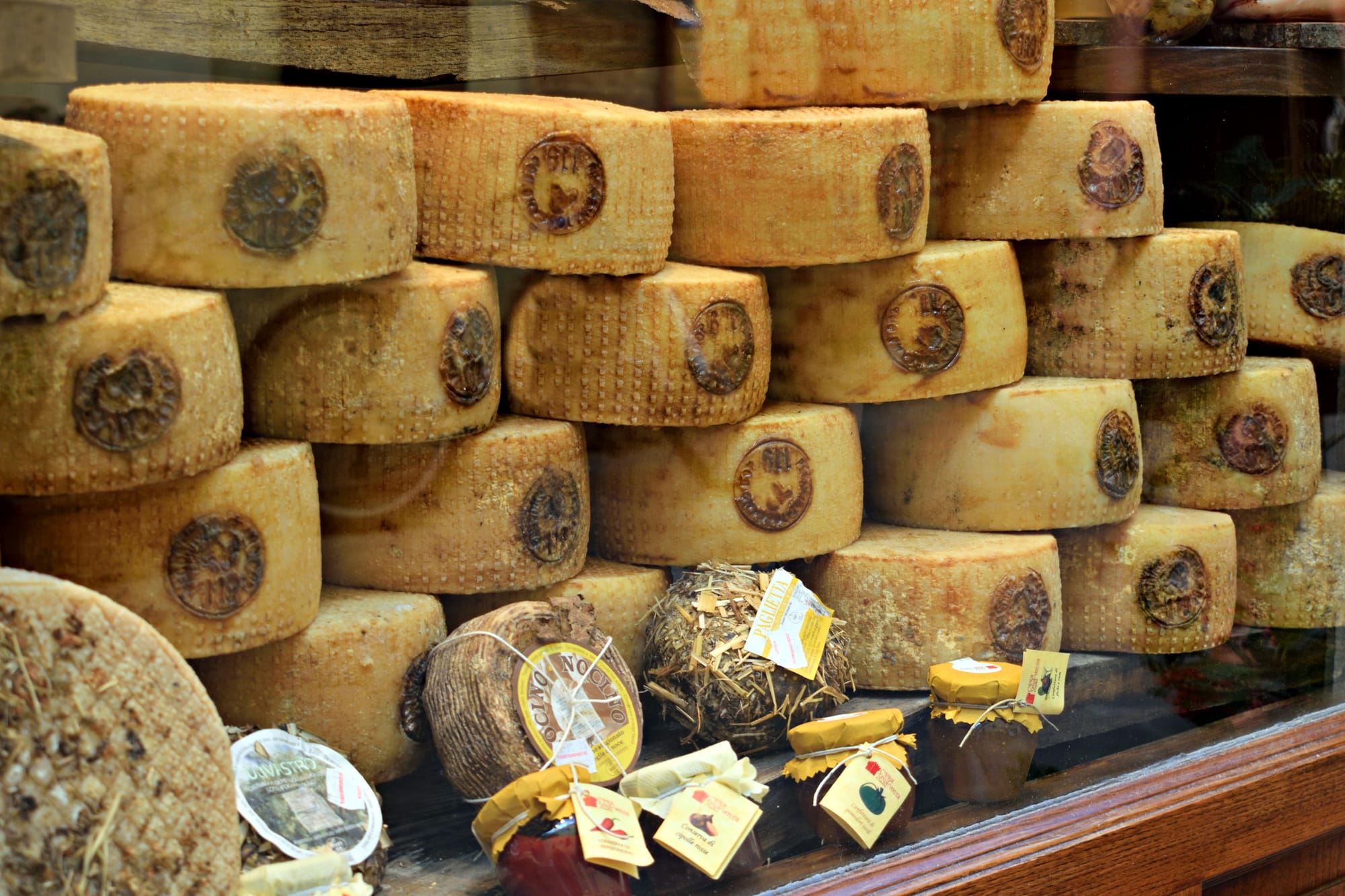 Wheels of artisan Pecorino di Pienza cheese aging on wooden shelves in a traditional shop in Tuscany.