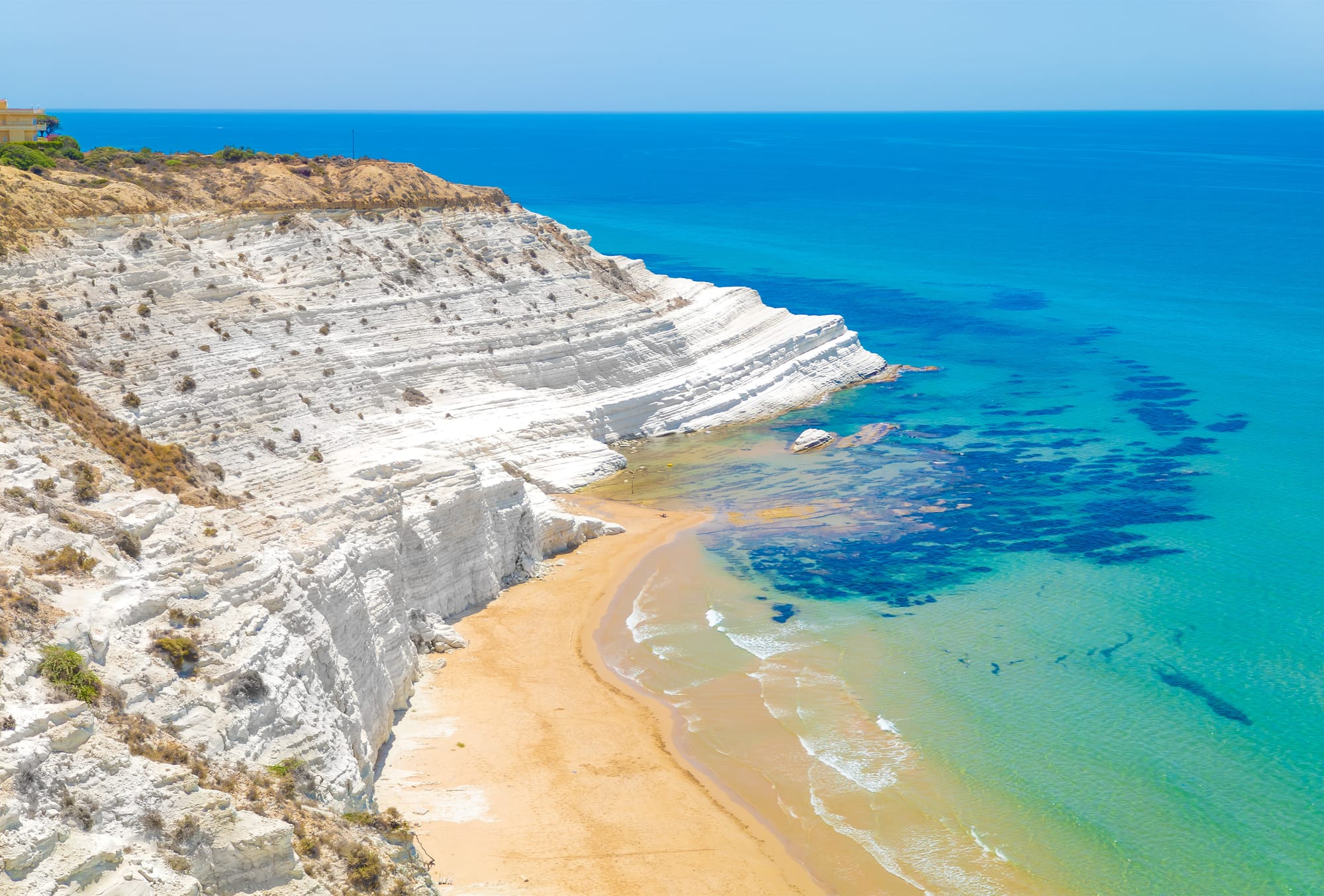 Aerial drone view of Scala dei Turchi near Realmonte, Sicily. The image shows the iconic white marl cliffs, golden sand beaches, and the deep blue Mediterranean Sea.