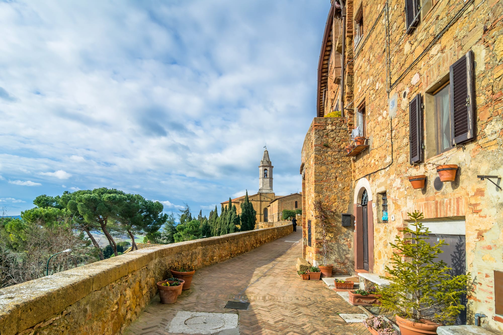 View of the Tuscan countryside from the panoramic walls of Pienza, with terracotta roofs and a church in the distance.