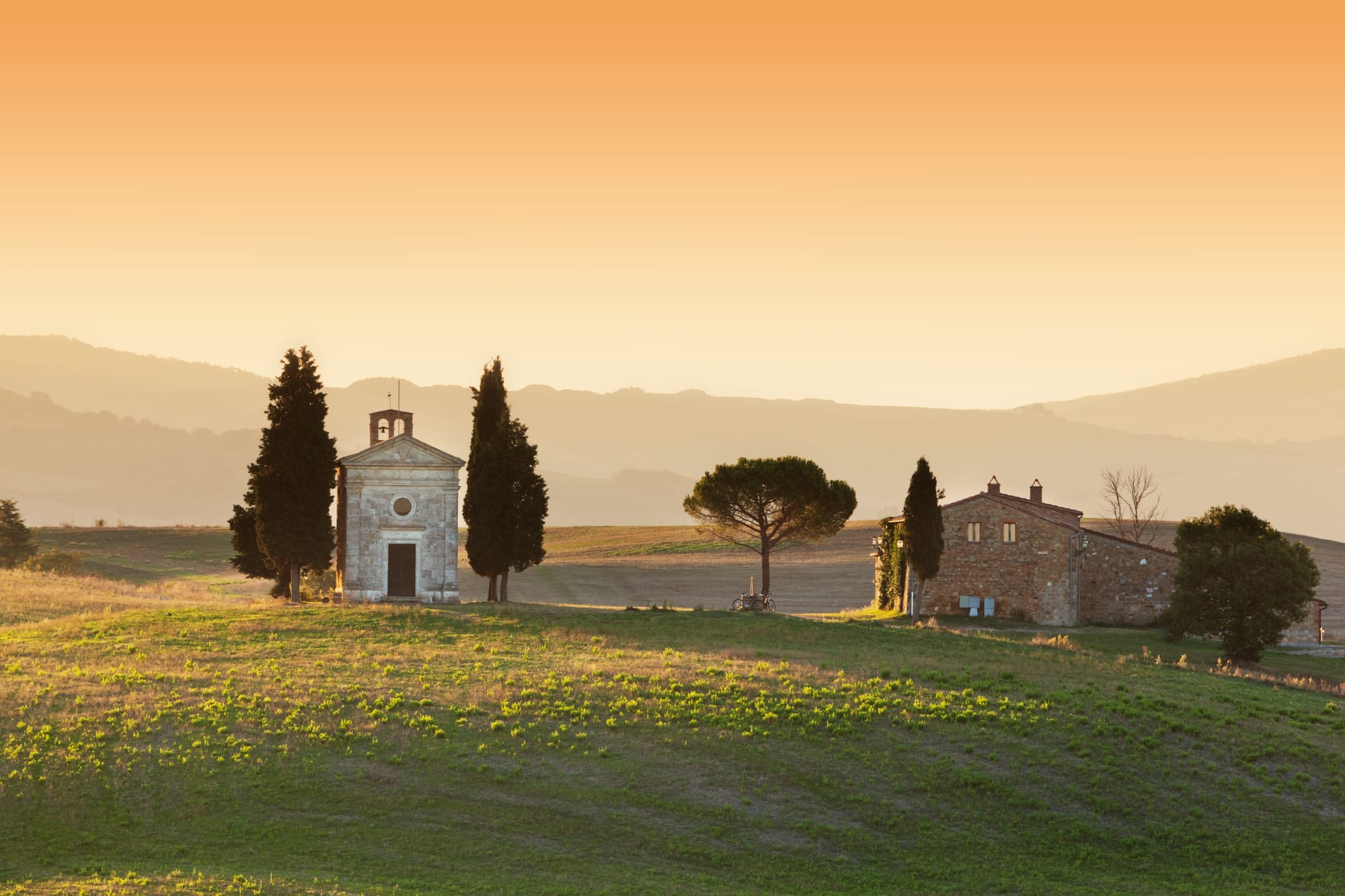 The solitary Chapel of Vitaleta flanked by two cypress trees on a hill in the Val d'Orcia, Tuscany, during a golden sunset.