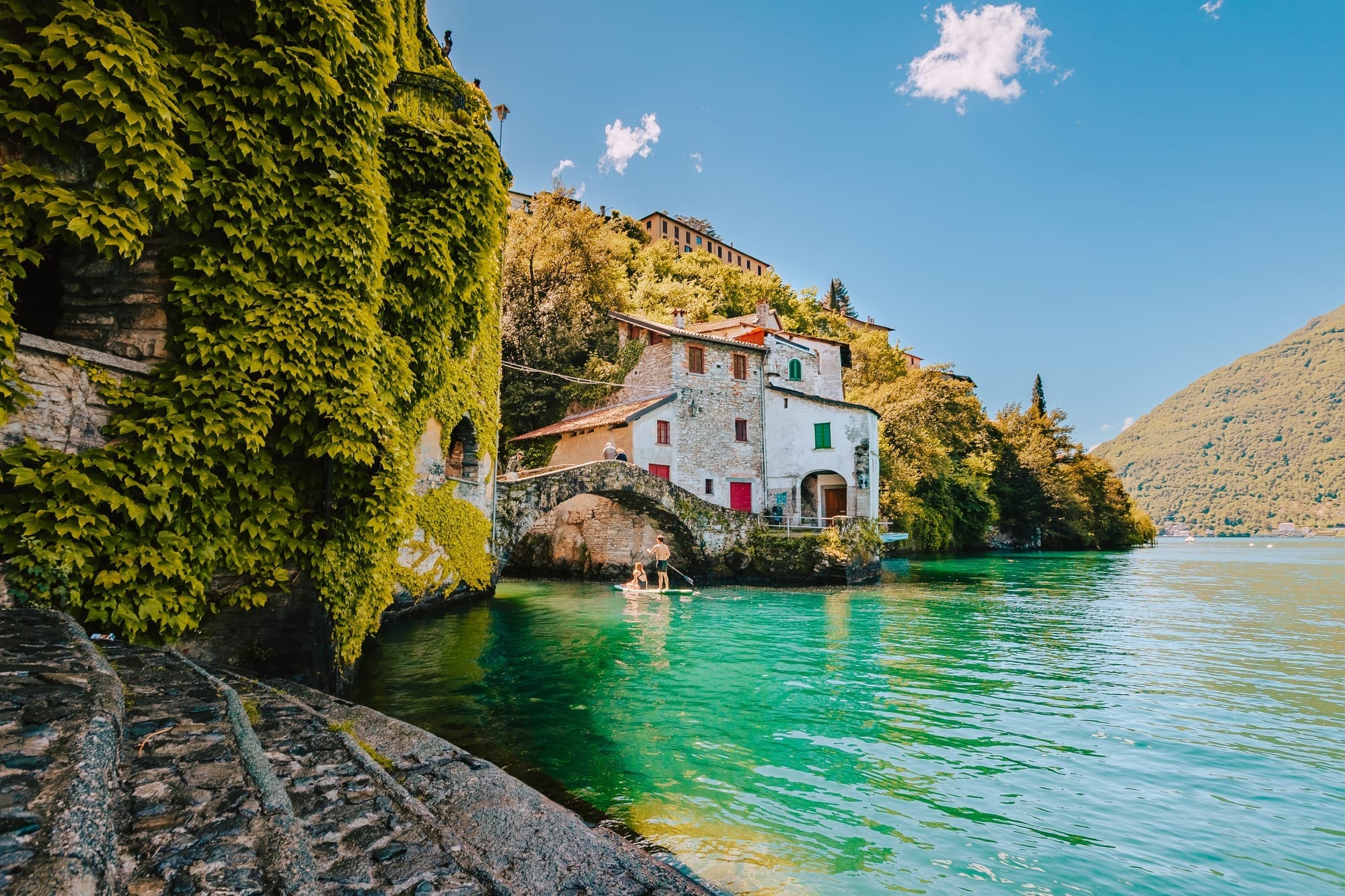 The historic stone Civera Bridge in Nesso, Italy, arching over the dramatic Orrido di Nesso waterfall and natural rock gorge.