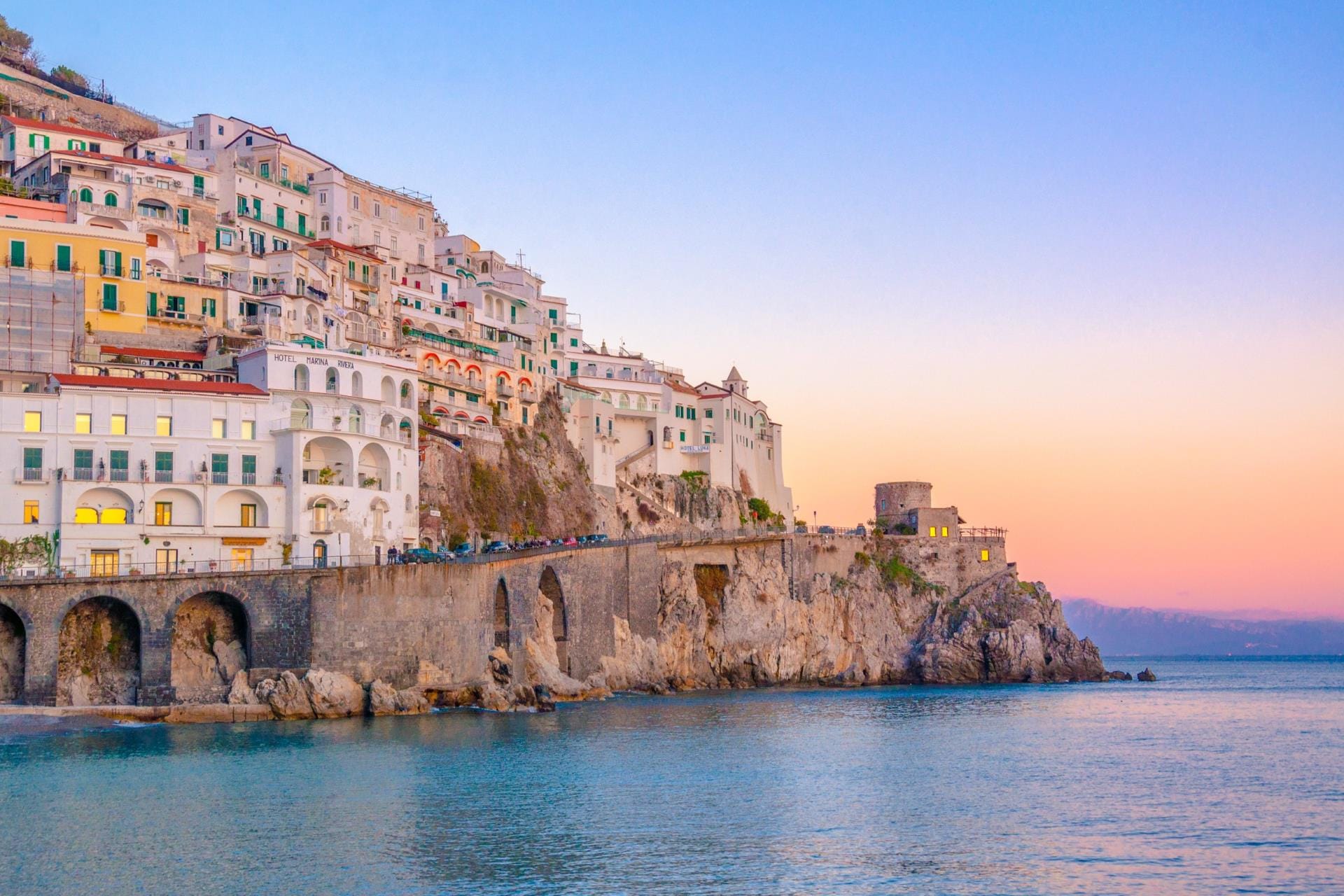 A dramatic sunset over the Amalfi coastline with the warm evening light reflecting on the Mediterranean Sea.