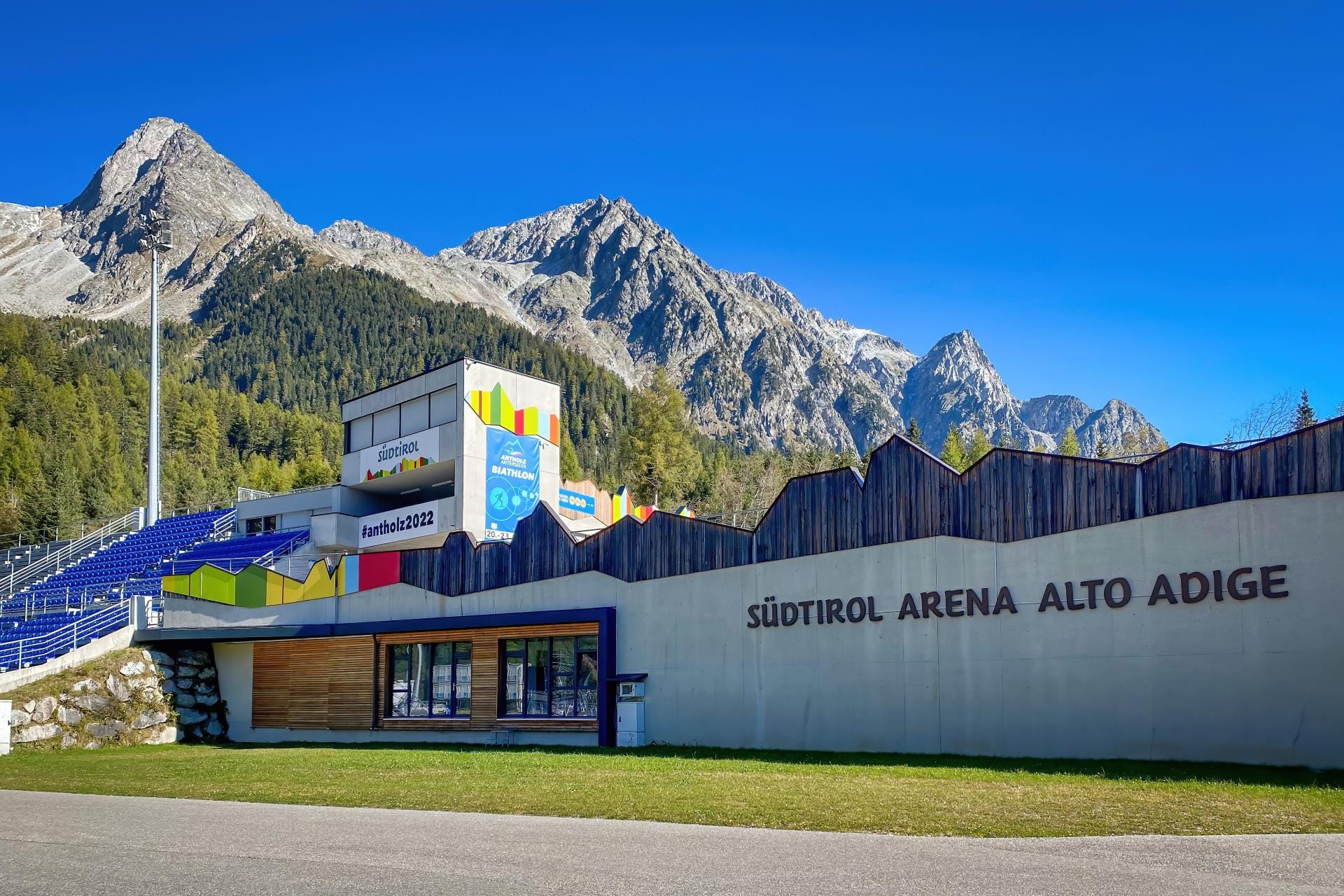 Panoramic view of the Südtirol Arena biathlon stadium in South Tyrol against a clear blue autumn sky.