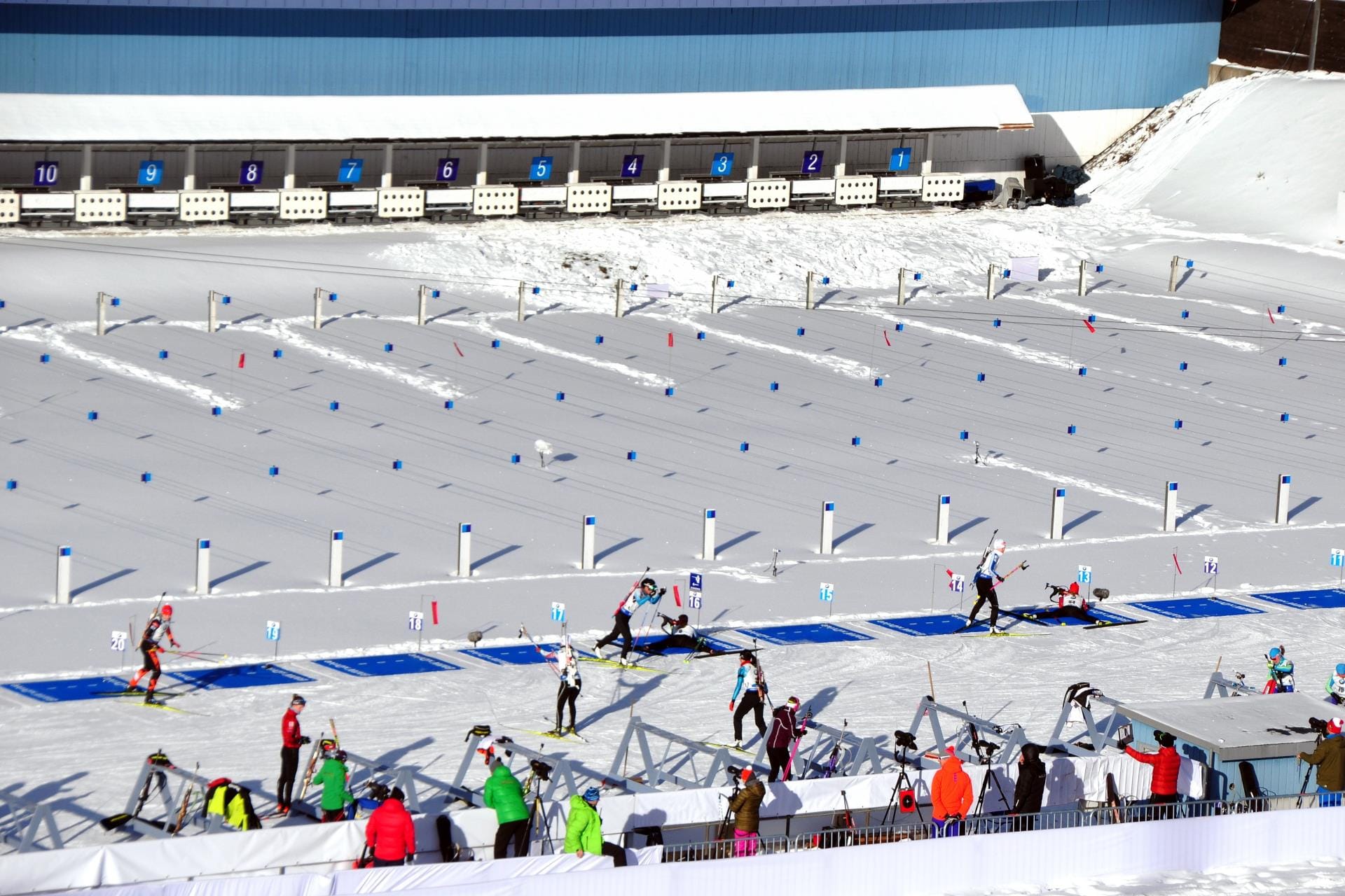 Busy activity at the biathlon shooting range with athletes practicing precision marksmanship in the Südtirol Arena.