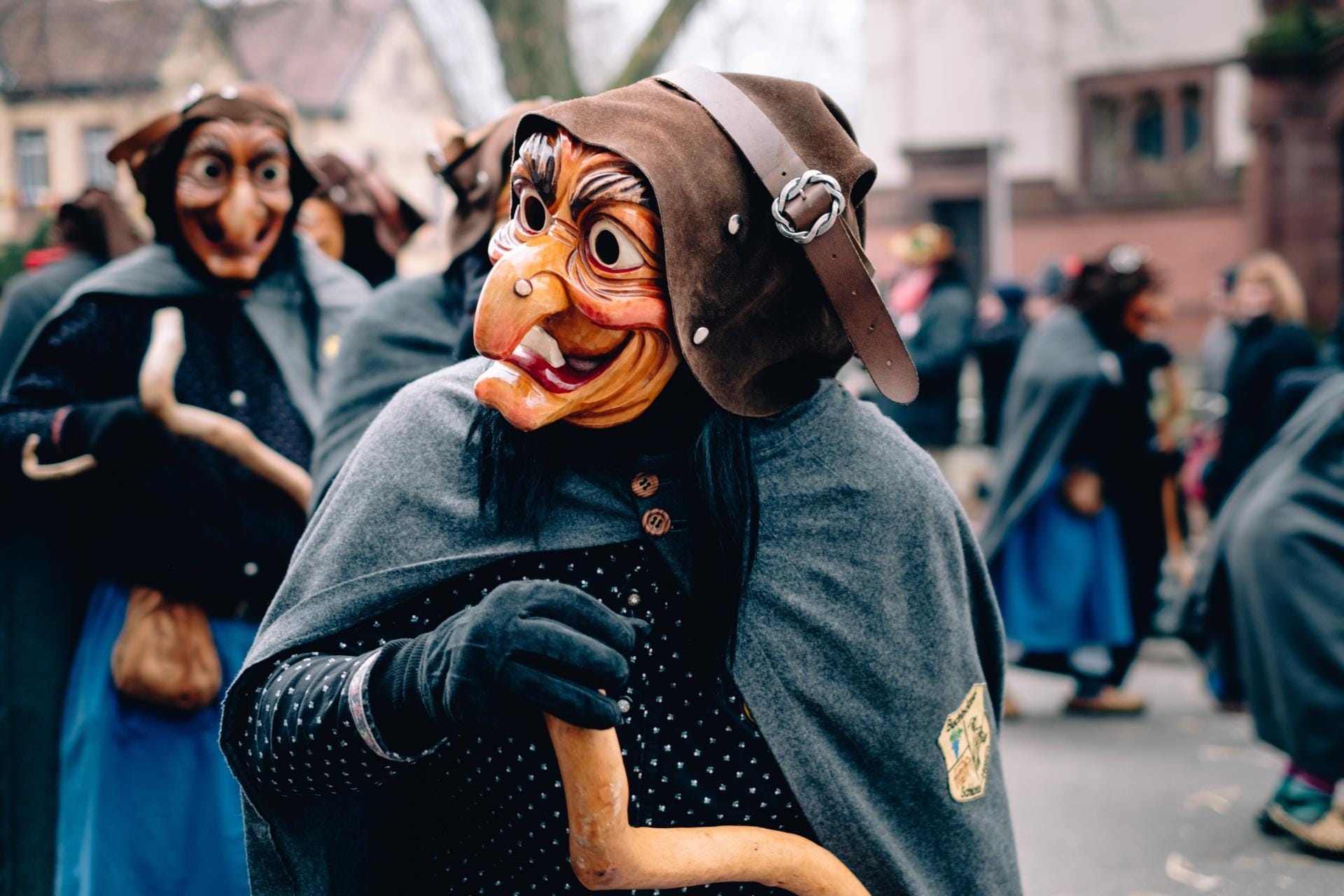 A person in a traditional La Befana costume and mask walking through an Italian cobblestone street during an Epiphany festival.