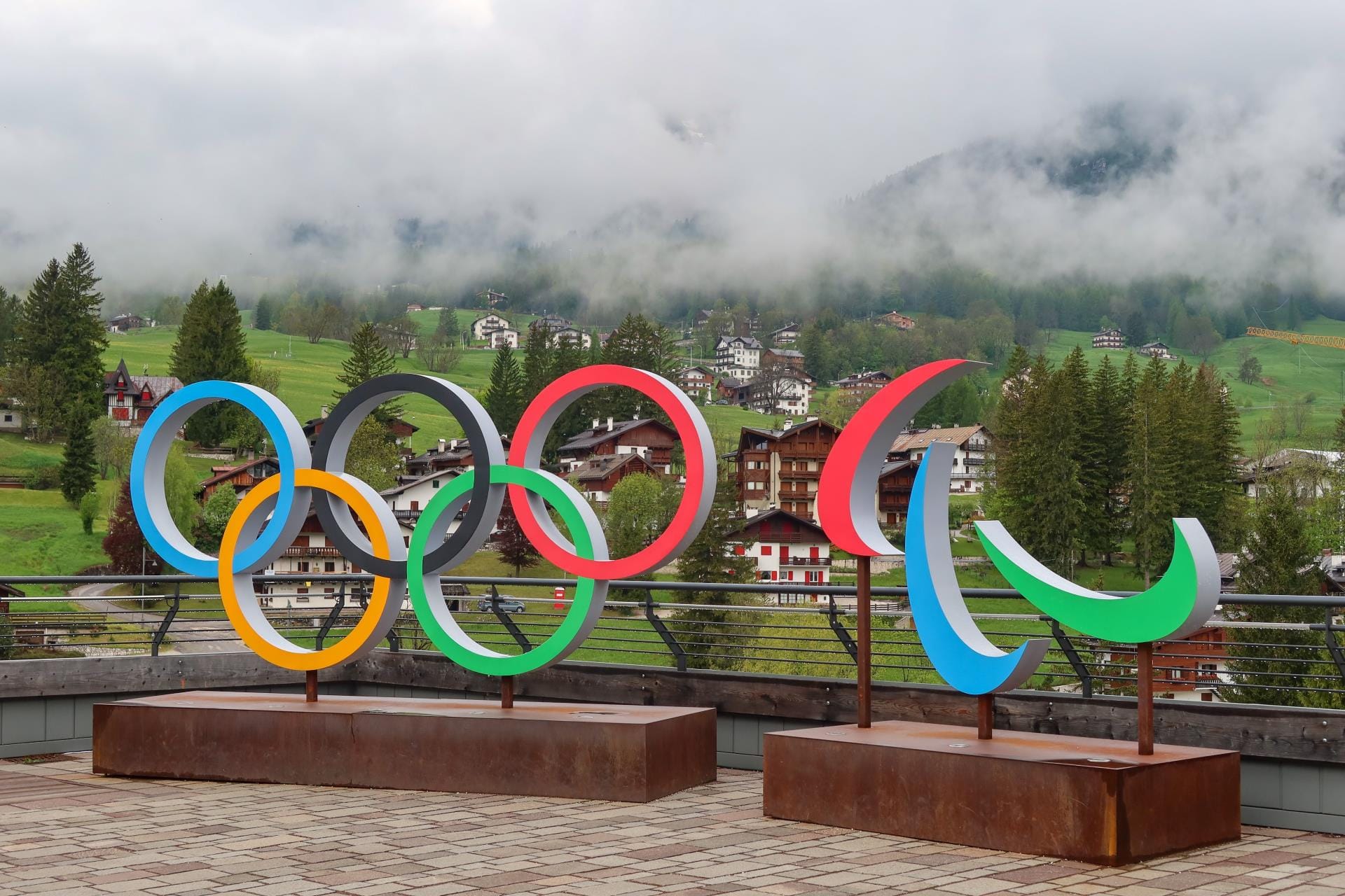 The Milano Cortina 2026 Olympic rings installation in the central square of Cortina d’Ampezzo with the jagged peaks of the Dolomites in the background.