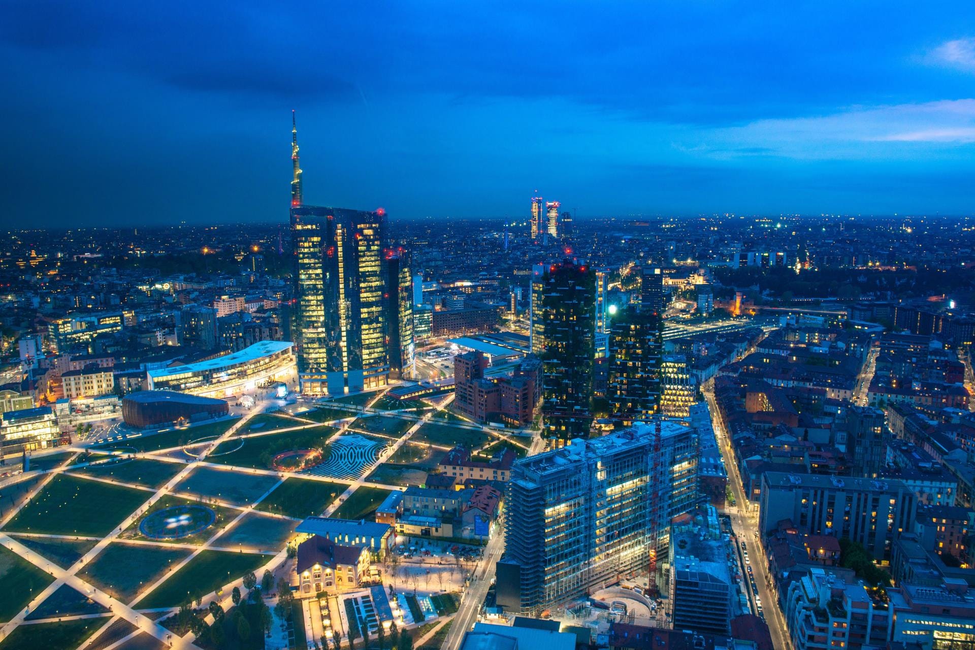 High-angle drone photograph of the modern Milan skyline at night, featuring Piazza Gae Aulenti and illuminated skyscrapers in the Isola district.