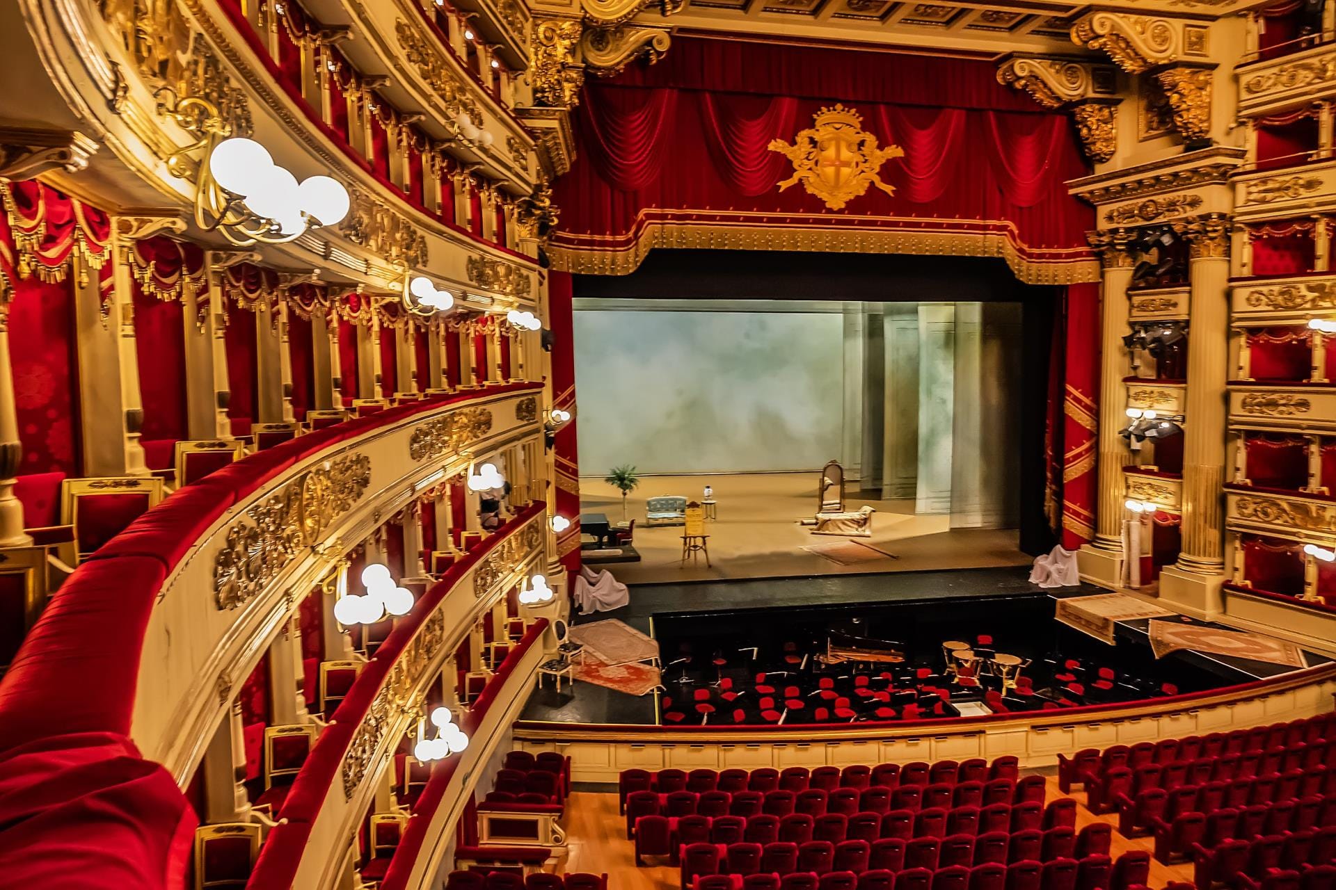 The opulent red-and-gold interior of the Teatro alla Scala opera house in Milan, showing the tiered boxes and the grand stage.