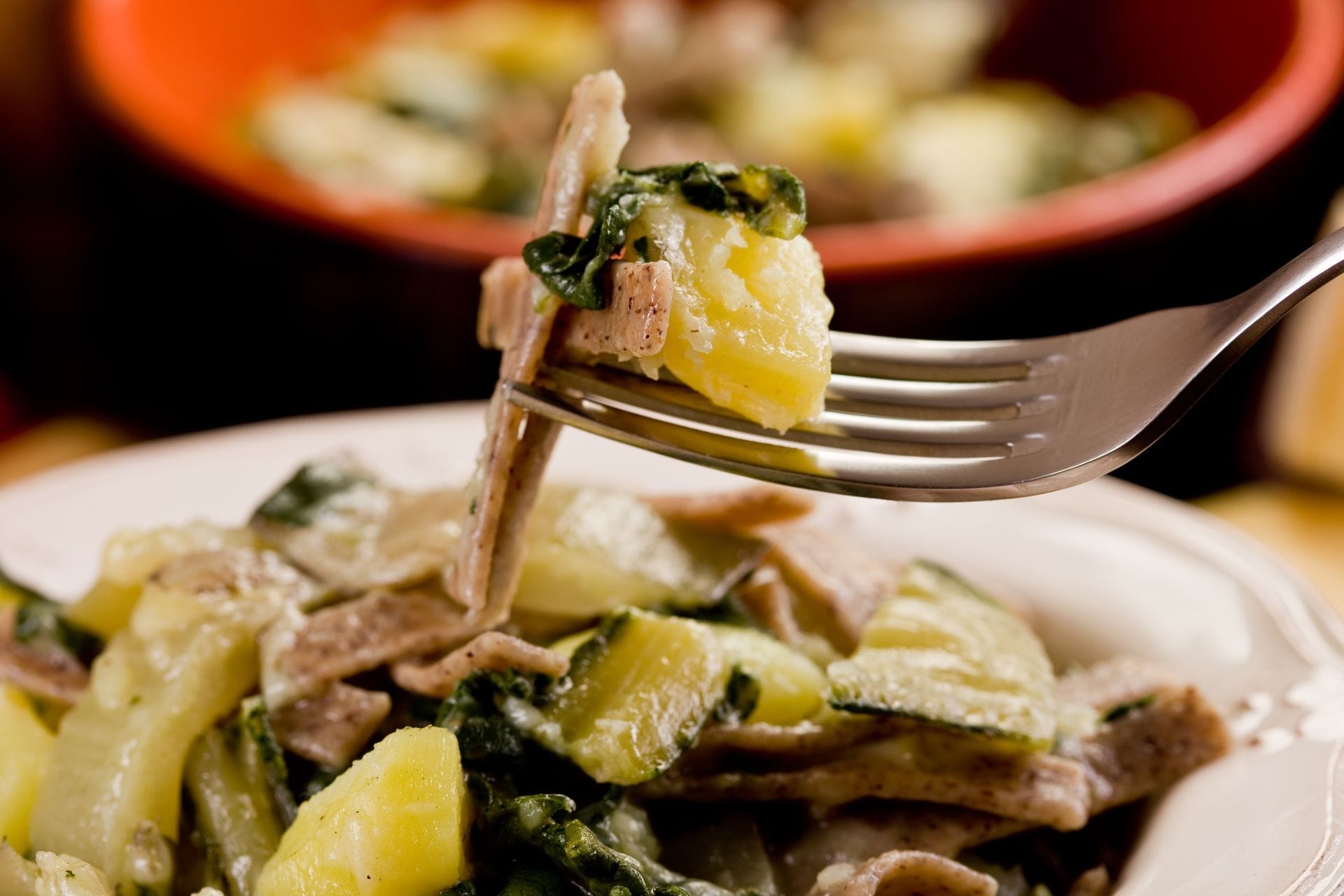 Close-up detail of a fork lifting steaming Pizzoccheri della Valtellina pasta with melted Casera cheese, potatoes, and cabbage.