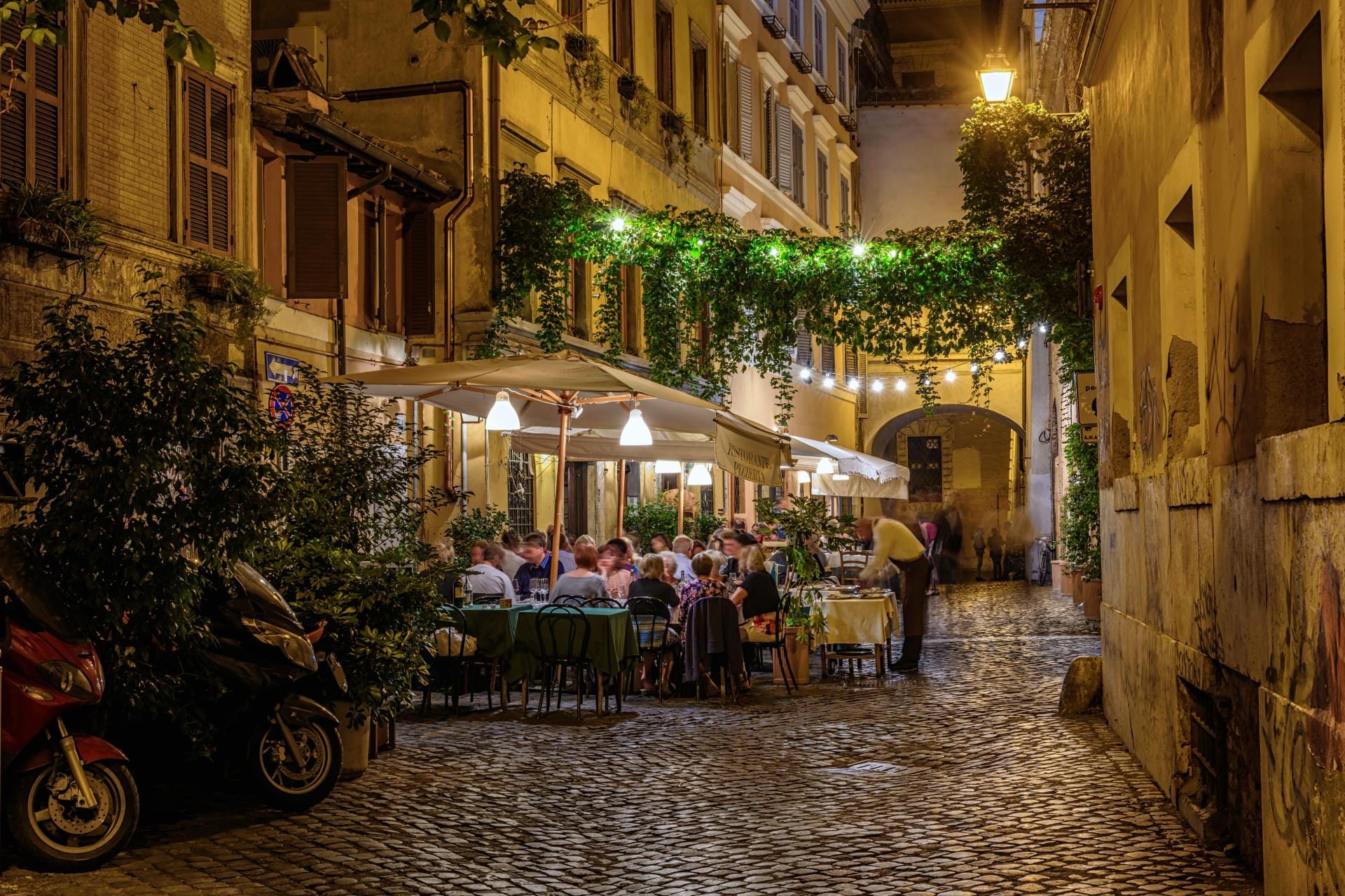 Outdoor dining tables at a traditional Roman trattoria in Trastevere at night.