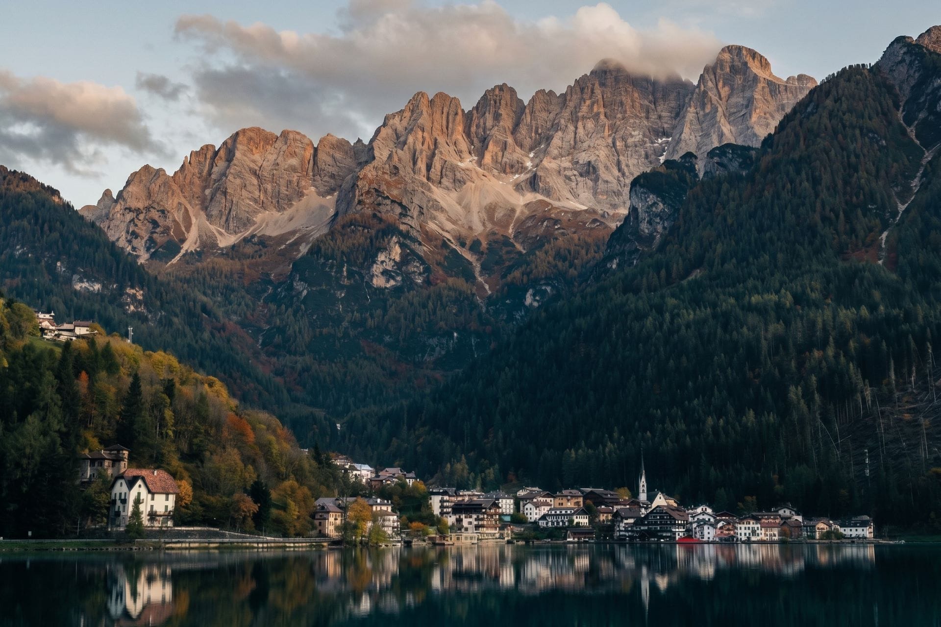 Panoramic summer view of Lago di Alleghe reflecting the surrounding towering peaks of the Italian Dolomites under a clear blue sky