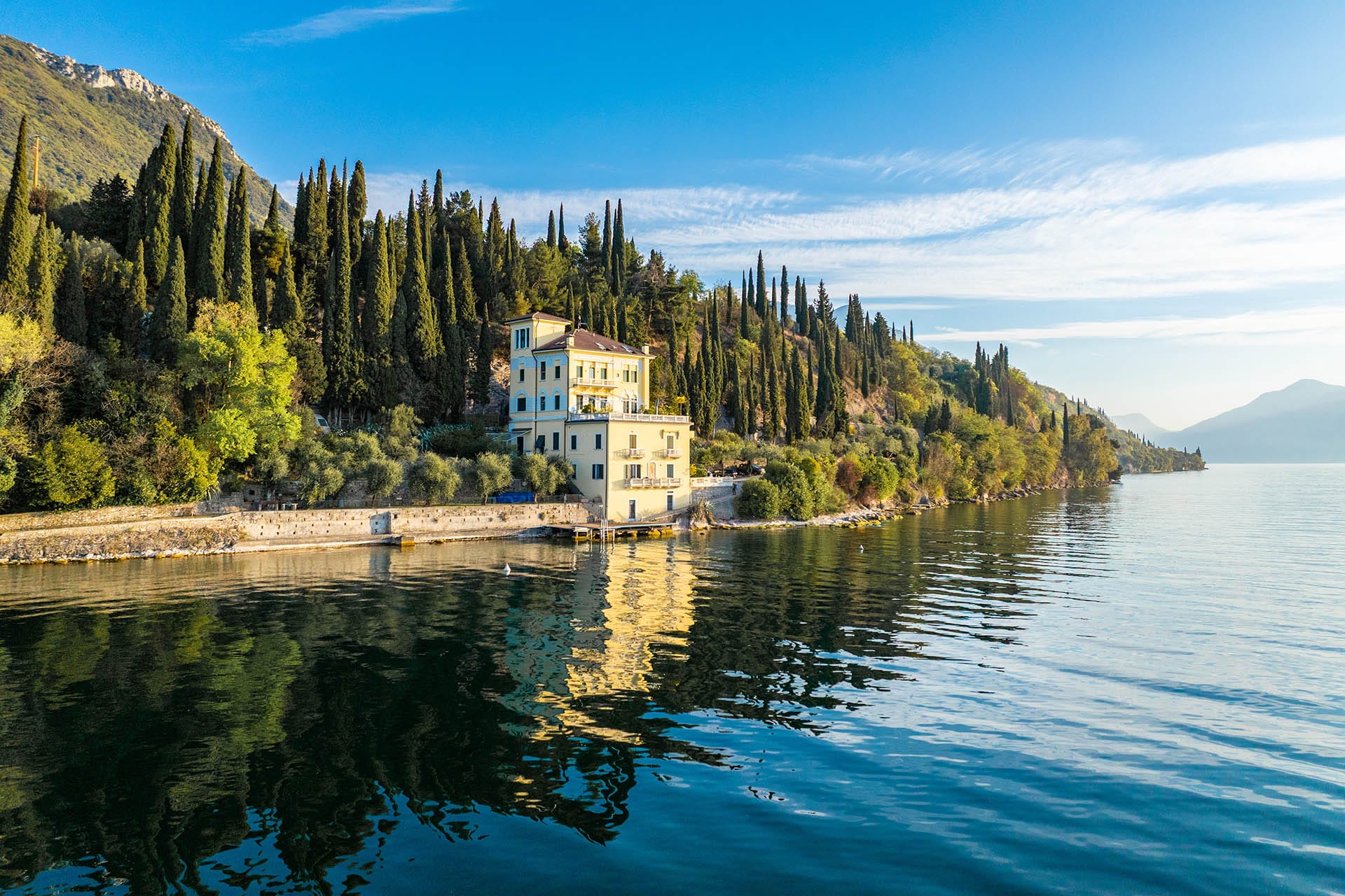 A historic Italian villa with terracotta facade and lush garden reflected in the still waters of Lake Garda near Gargnano, Lombardy, Italy