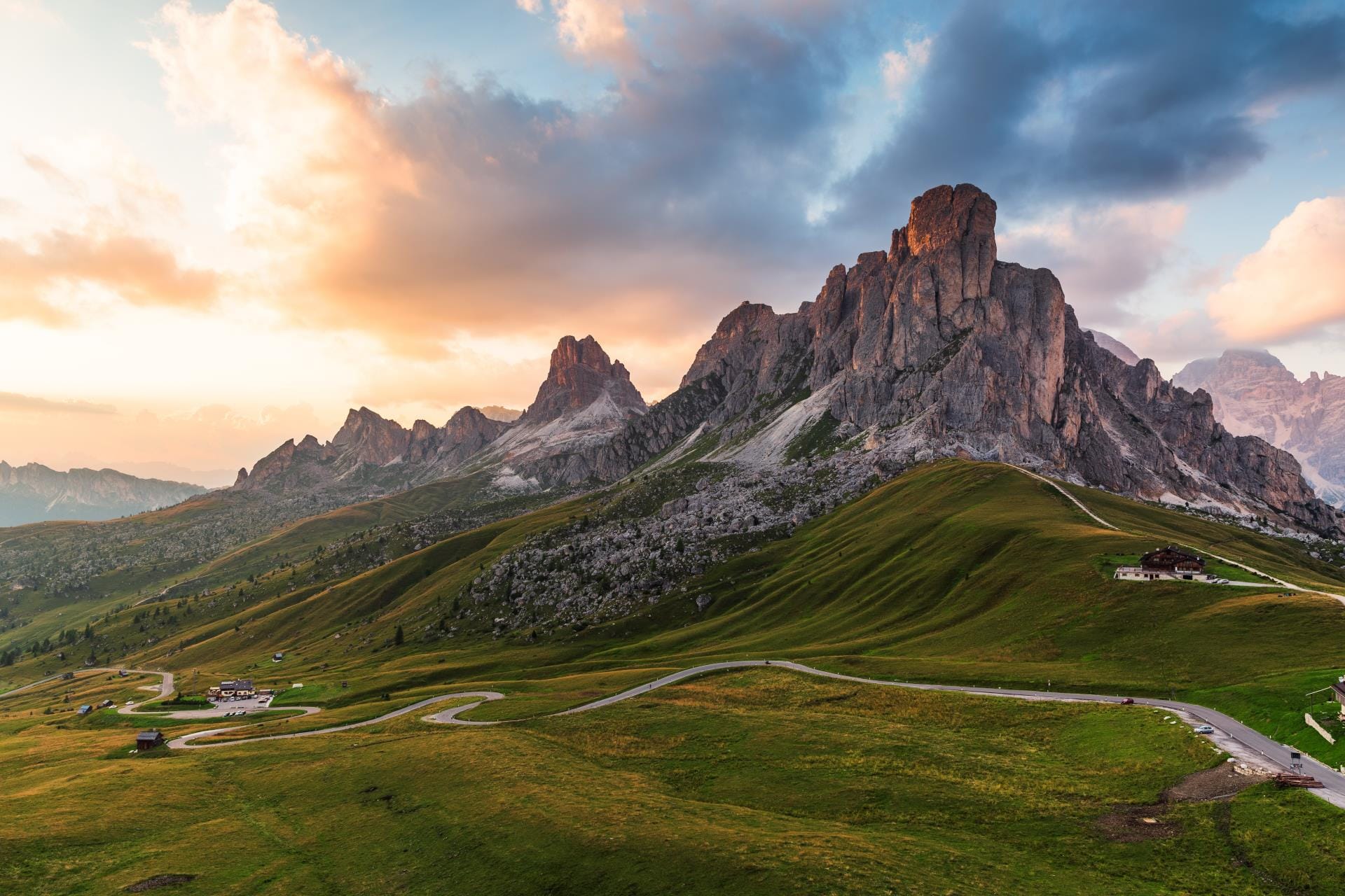 Sweeping panoramic view of the iconic Passo Giau in the Italian Dolomites, featuring lush green alpine meadows and dramatic jagged mountain peaks.