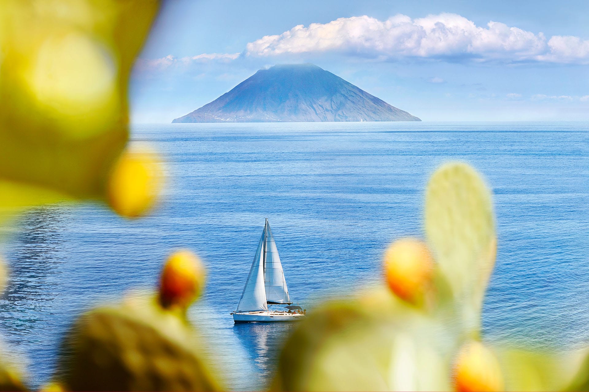 Panoramic view from Salina Island across the blue Tyrrhenian Sea toward the active Stromboli volcano rising from the water, Aeolian Islands, Sicily, Italy.