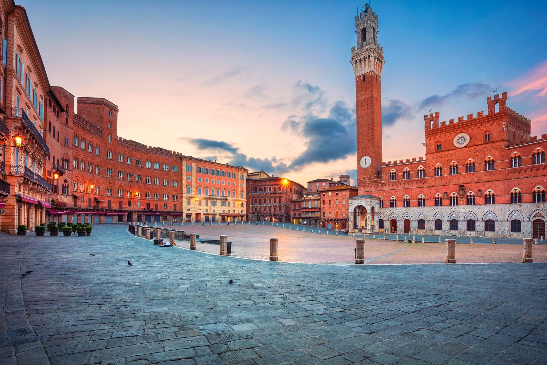 Panoramic cityscape of Siena at sunrise with the iconic shell-shaped Piazza del Campo and the Torre del Mangia rising above the medieval rooftops, Tuscany, Italy.