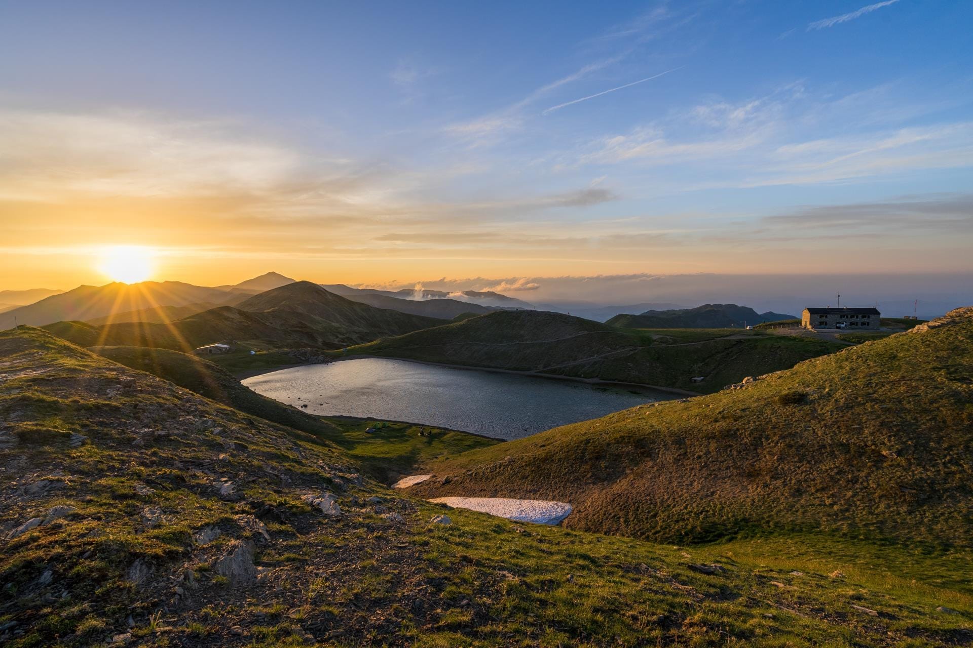 Golden hour sunset illuminating the lush green valleys and rugged peaks of the Corno alle Scale mountain range in the Italian Apennines.