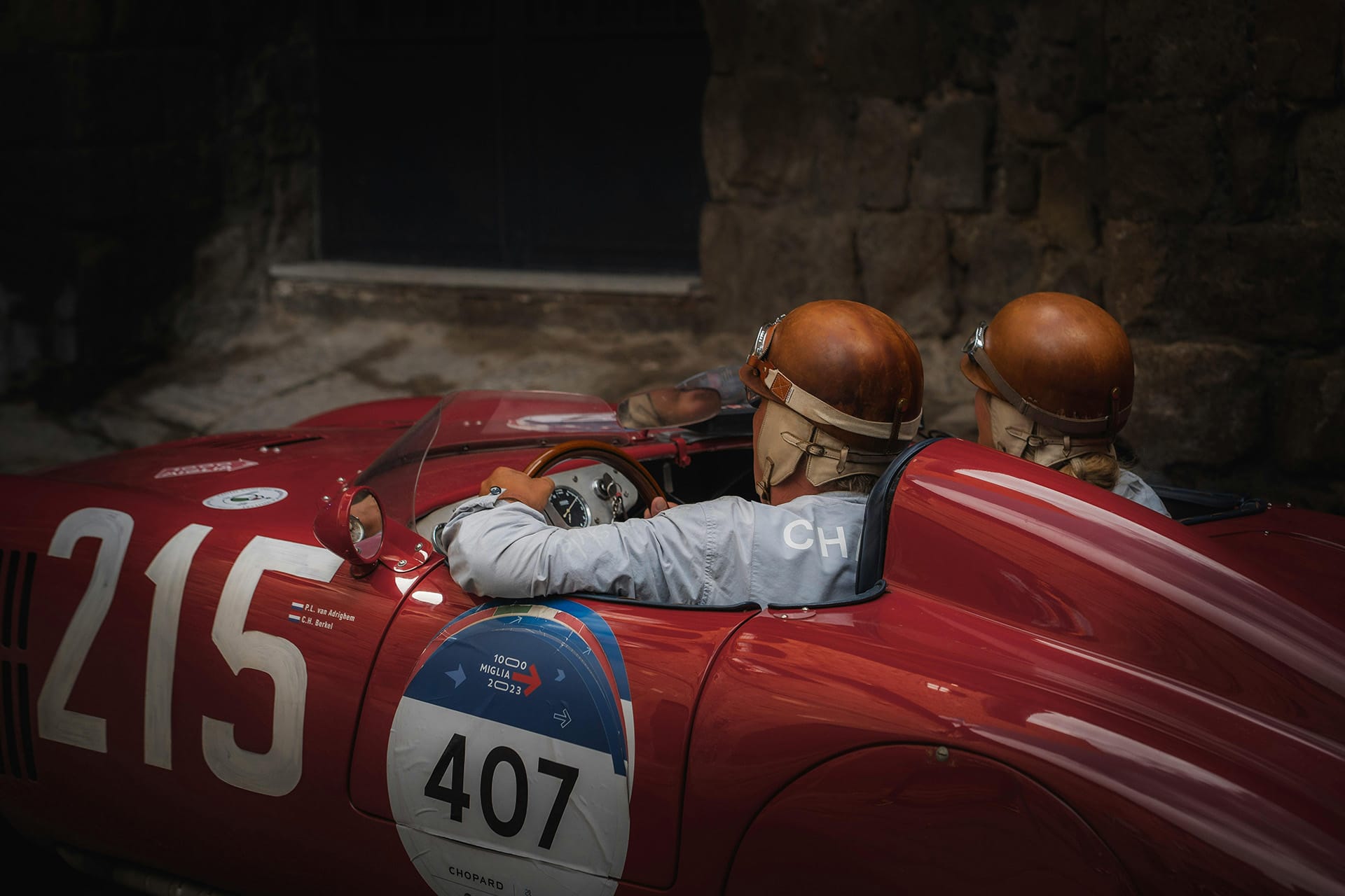 Two crew in leather helmets in a red car on the modern 1000 Miglia re-enactment in 2023
