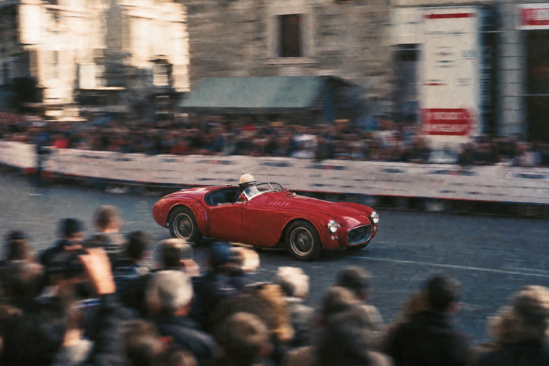 Red postwar sports barchetta racing past a crowd lining a town street during the Mille Miglia