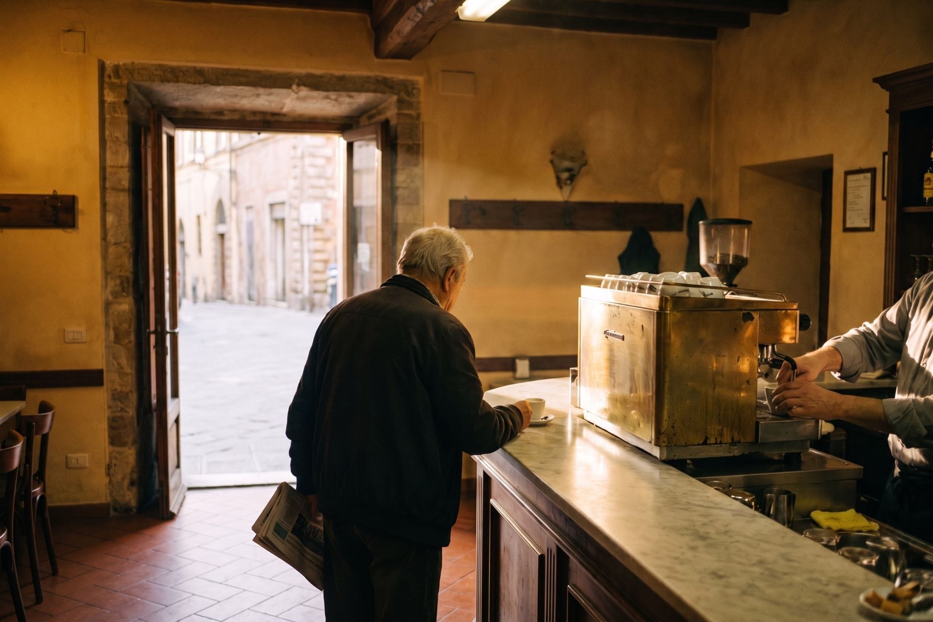  Elderly man drinking espresso at the marble counter of a traditional bar in Siena