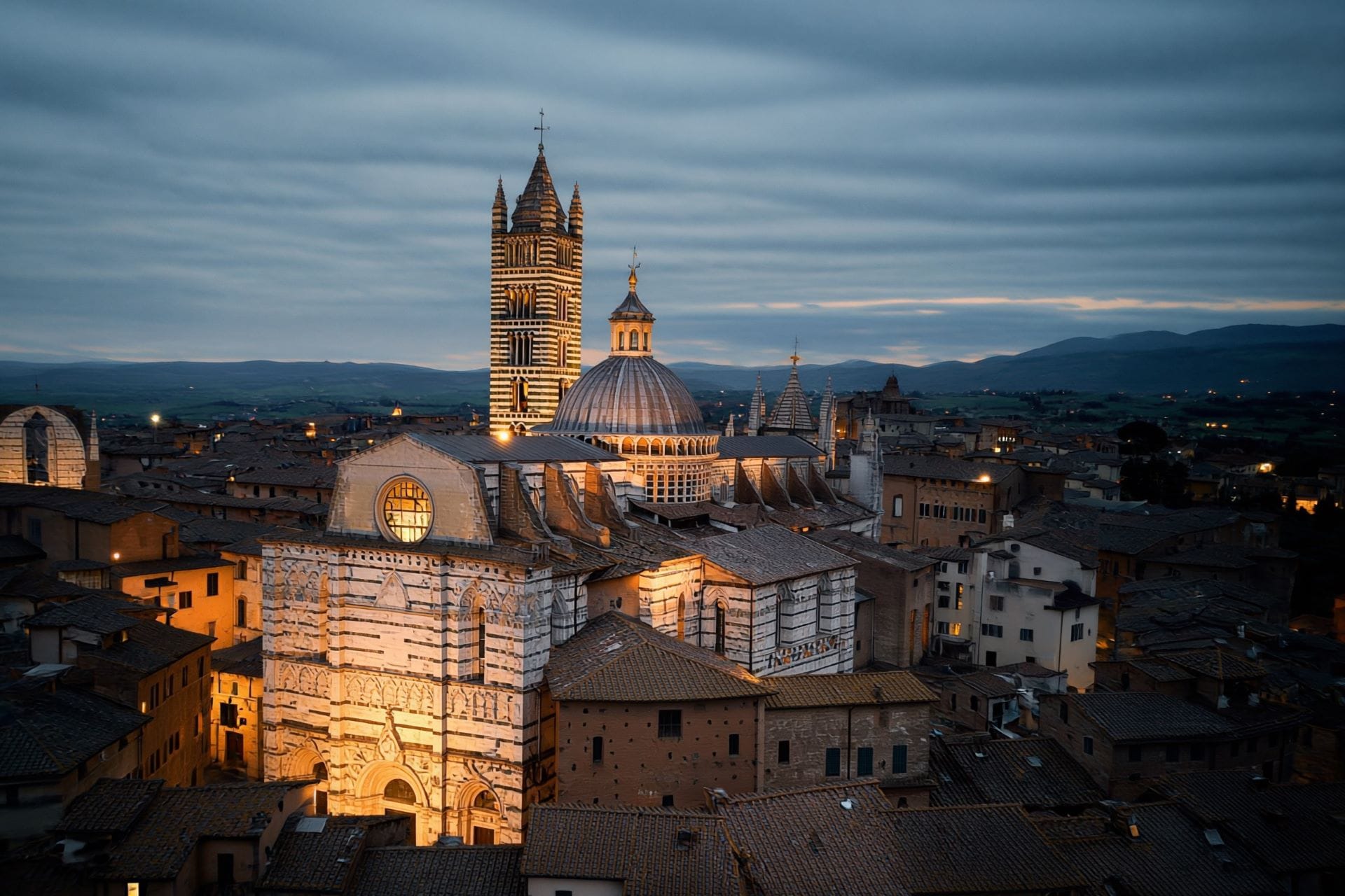 Siena Cathedral dome and striped bell tower above the rooftops at dusk