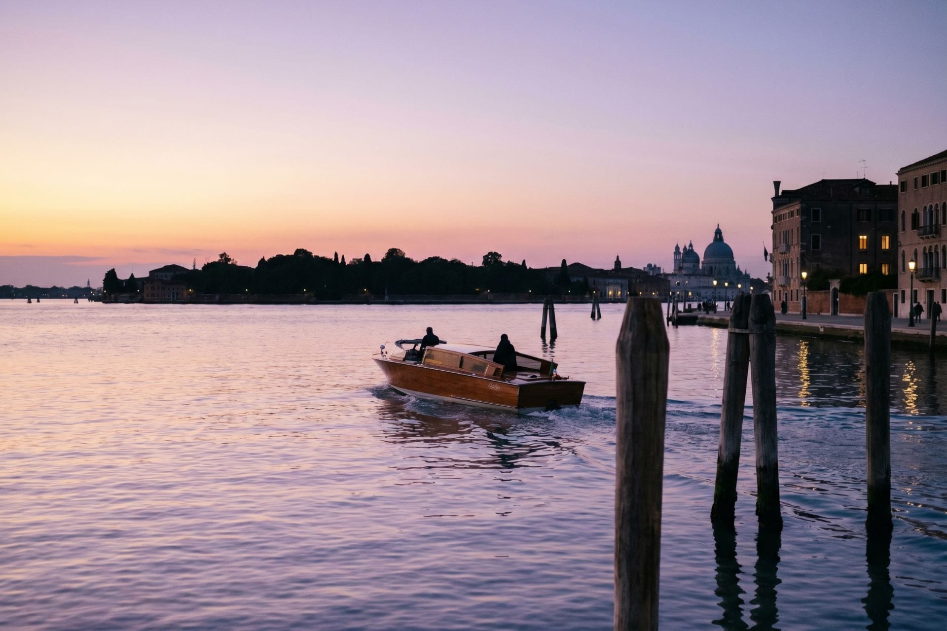 A wooden water taxi on the Venice lagoon at dusk with the dome of Santa Maria della Salute behind