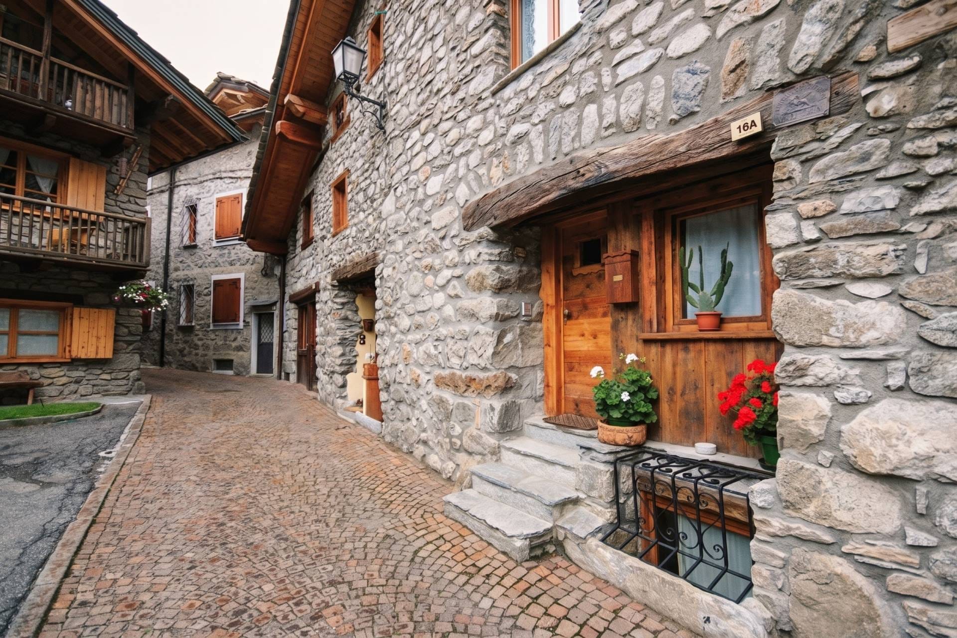 Traditional alpine stone houses with wooden doors and red geraniums along a narrow cobbled street in Courmayeur.