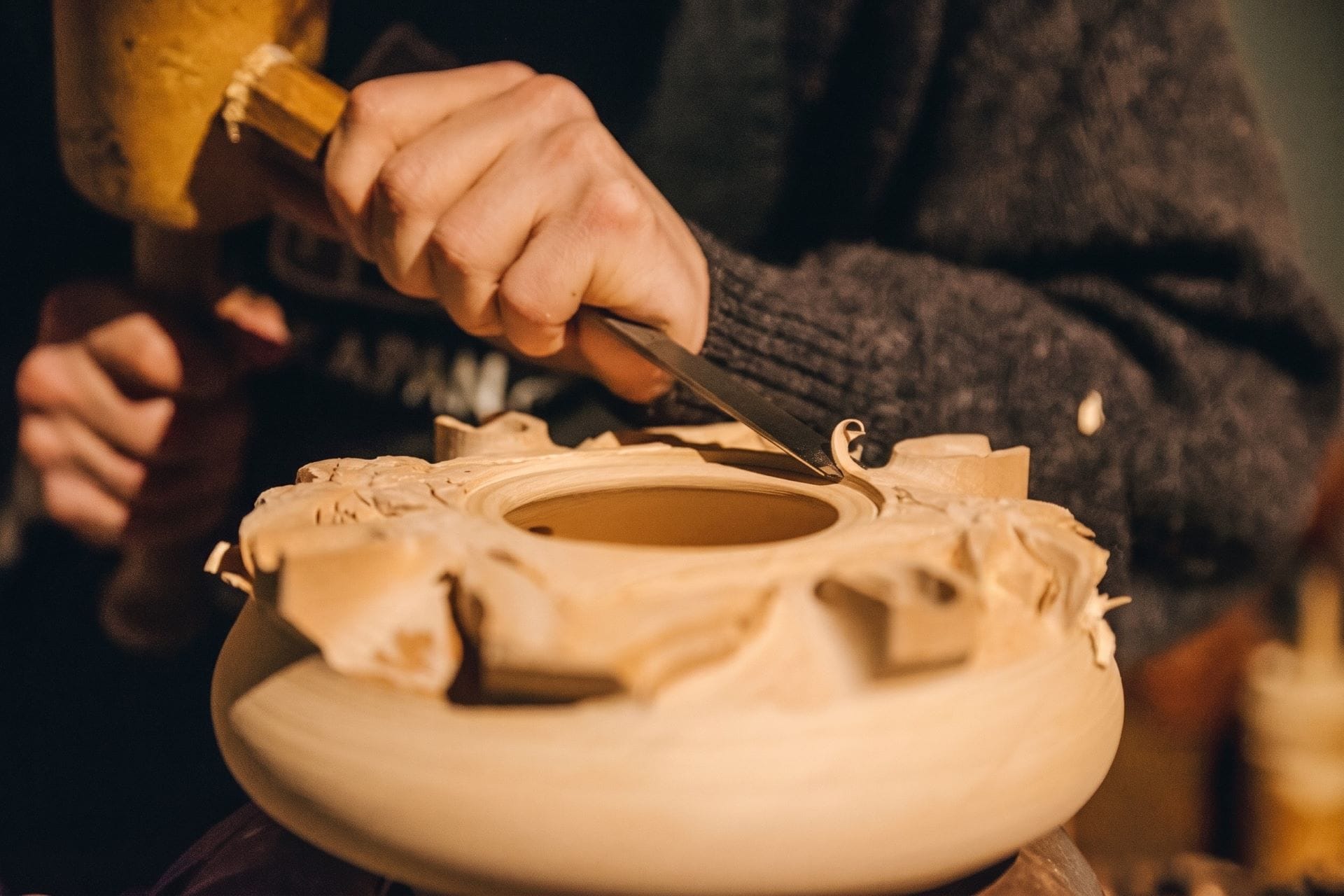 Valdostan woodcarver hollowing a turned wooden bowl with a gouge and mallet in a workshop