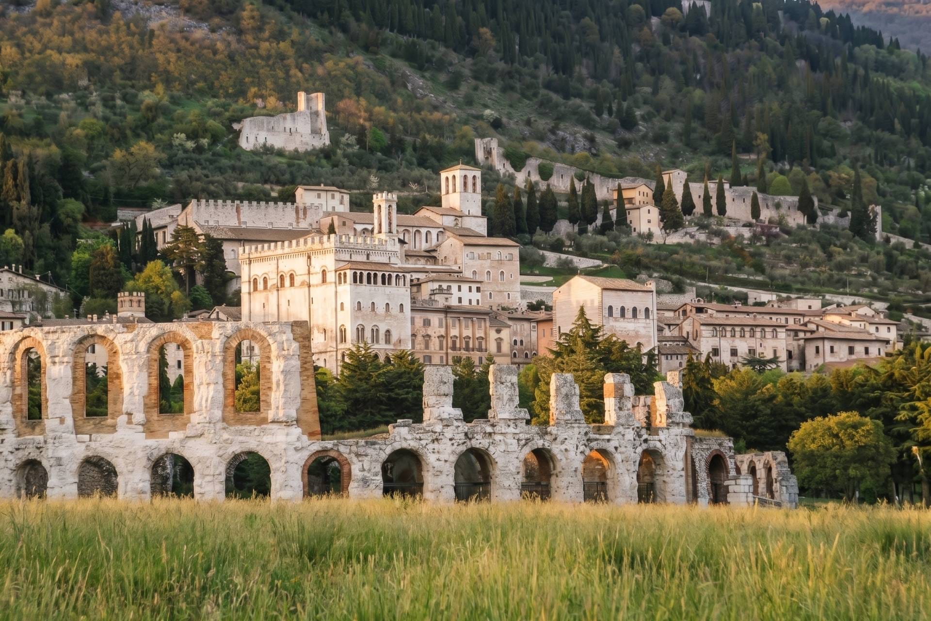 Gubbio's Roman theatre ruins below the medieval town and Palazzo dei Consoli in golden light, Umbria