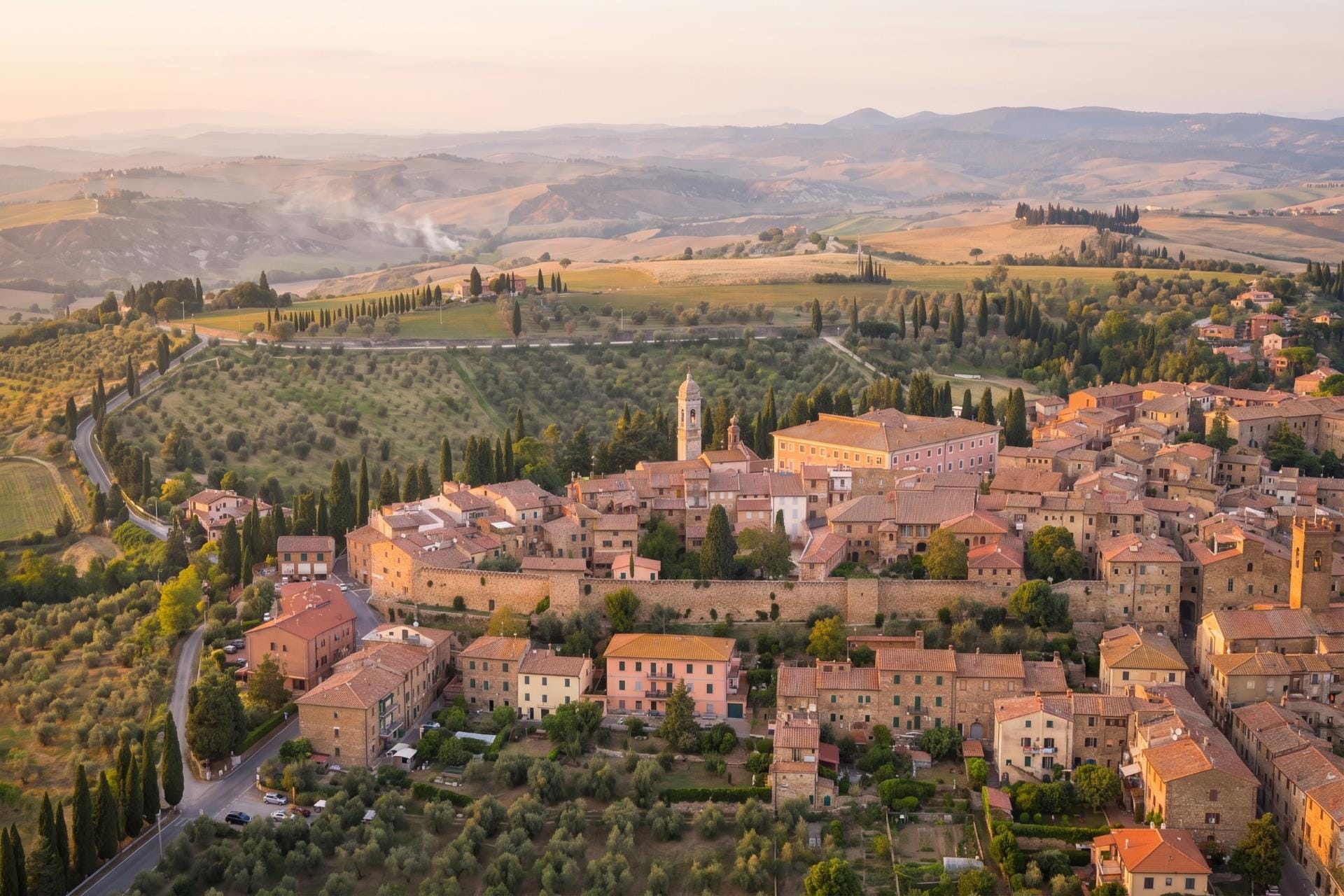 San Quirico d'Orcia, a walled Val d'Orcia hill town and bell tower above olive groves at dawn