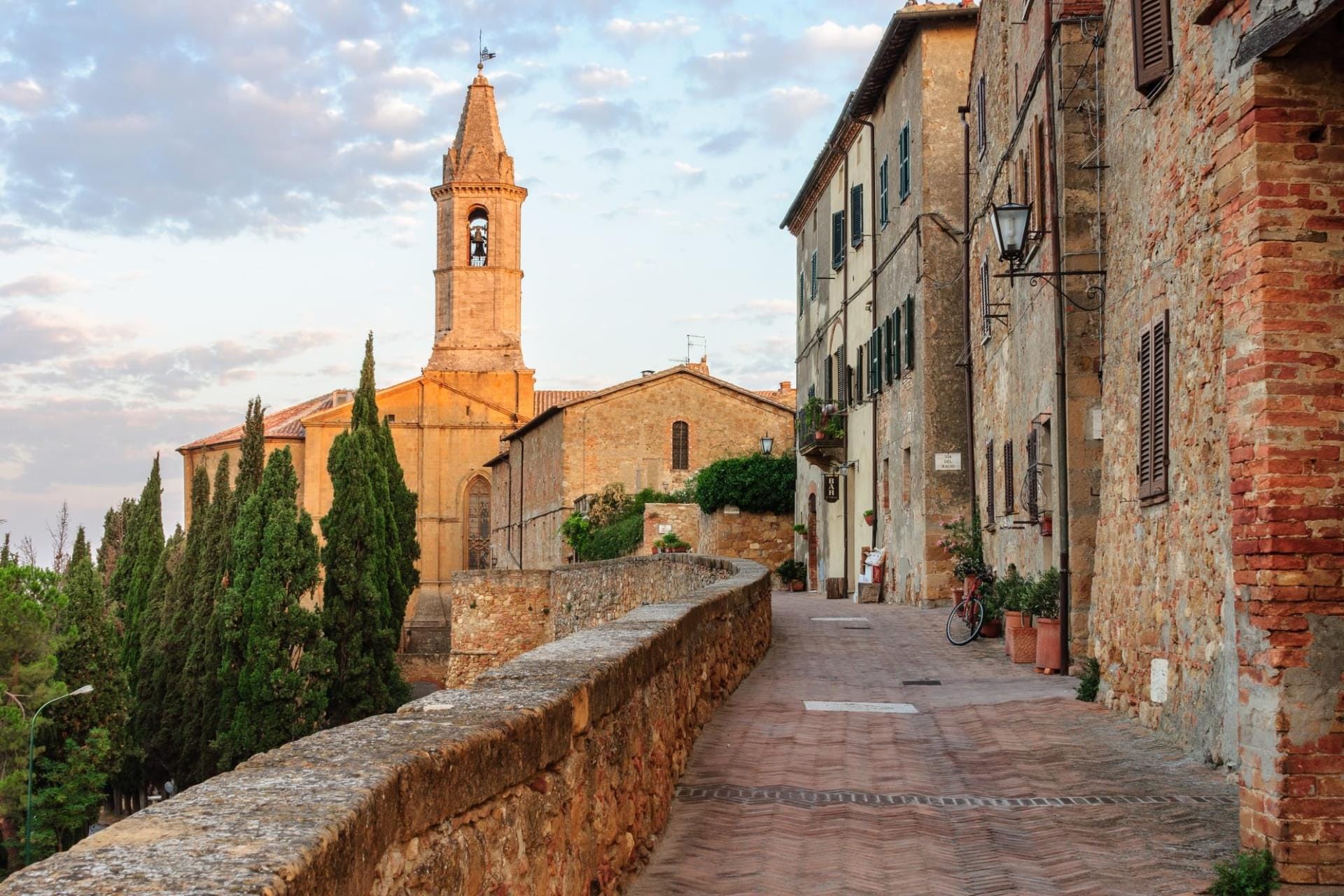 Pienza cathedral bell tower above a brick-paved lane at golden hour, Val d'Orcia
