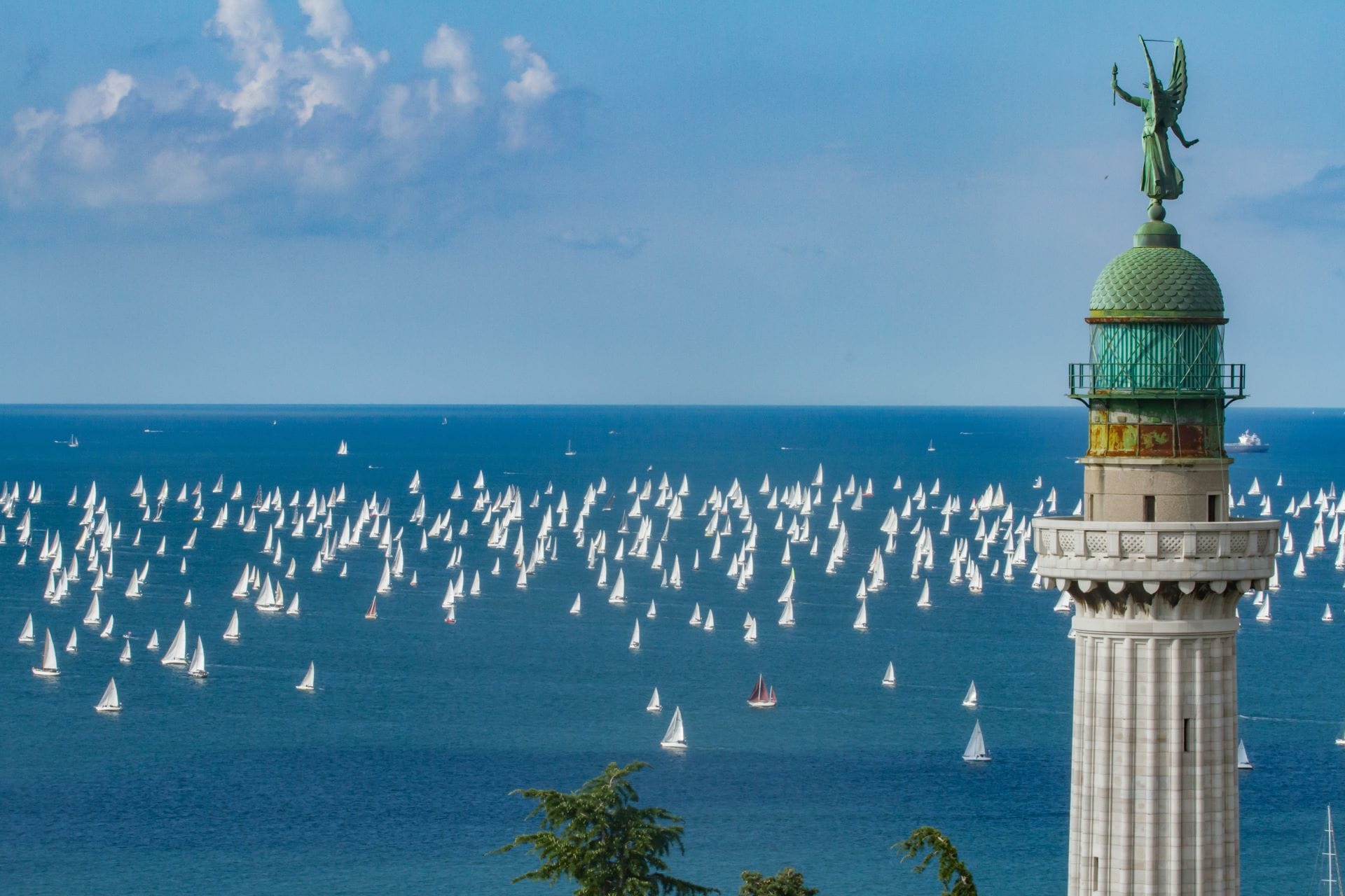 Hundreds of sailboats racing past the Faro della Vittoria lighthouse during the Barcolana regatta in Trieste