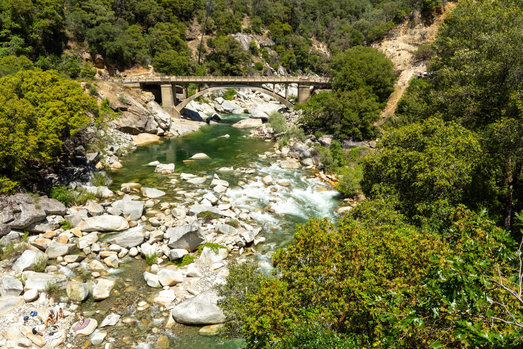 Yuba River flowing through Sierra Nevada canyon with clear water, large granite boulders, and stone bridge amid green vegetation.