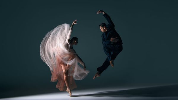 Ballet couple moving in synchronised dramatic jump with flowing dress motion. Concept of energy, passion, performing arts, fluid choreography, emotional harmony and cultural expression.