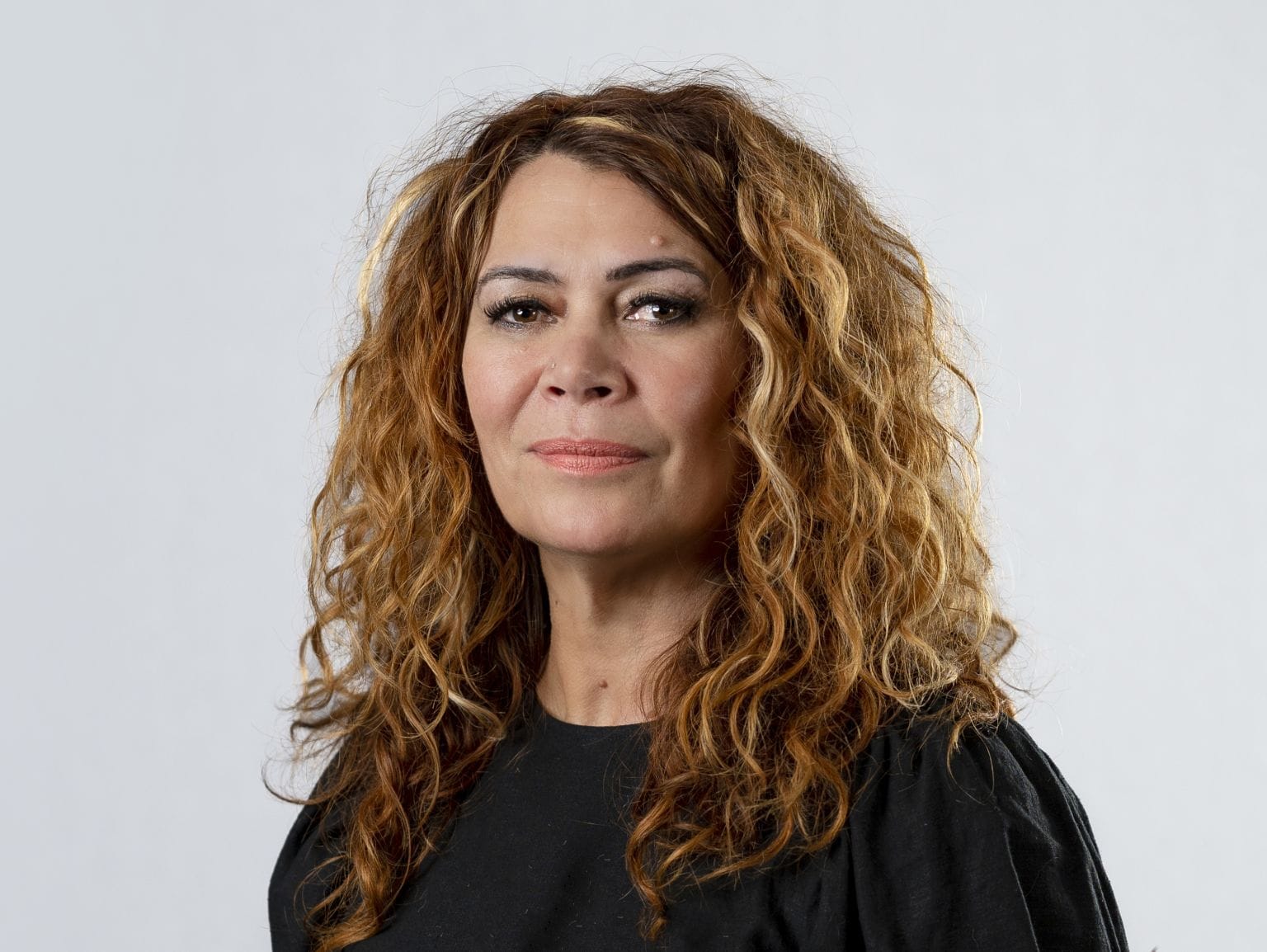 Head and shoulders shot of Antoinette Braybrook. She has light brown skin, sandy brown curly hair and is smiling reservedly. She is wearing a black top.
