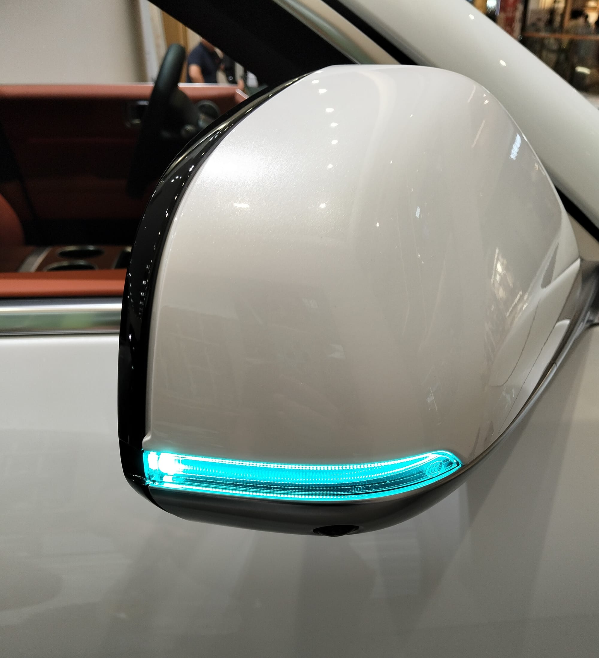 Right side-view mirror of a car with one row of turquoise lights around the corner