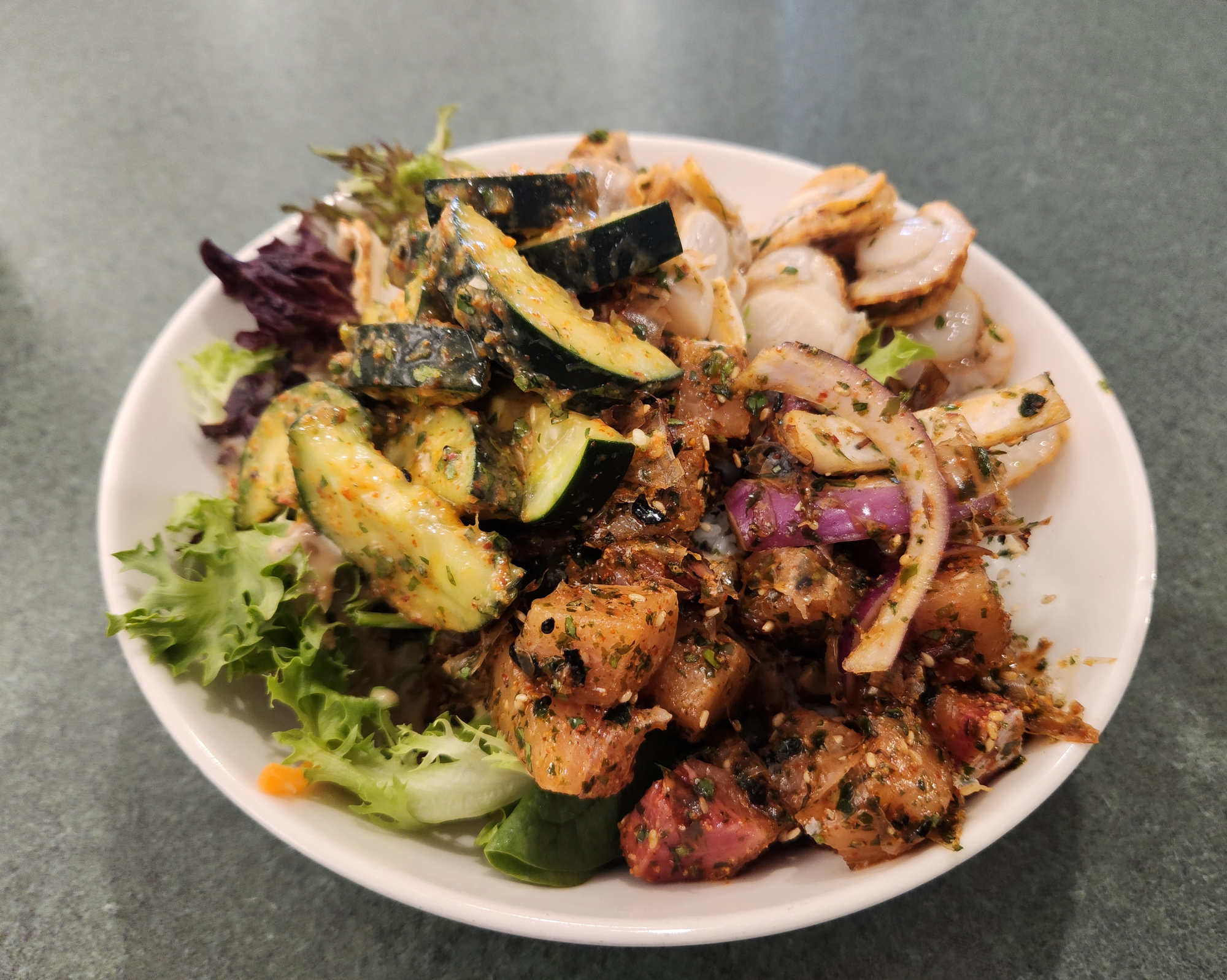 A very full bowl of poke with scallops, tuna, and miso cucumbers.