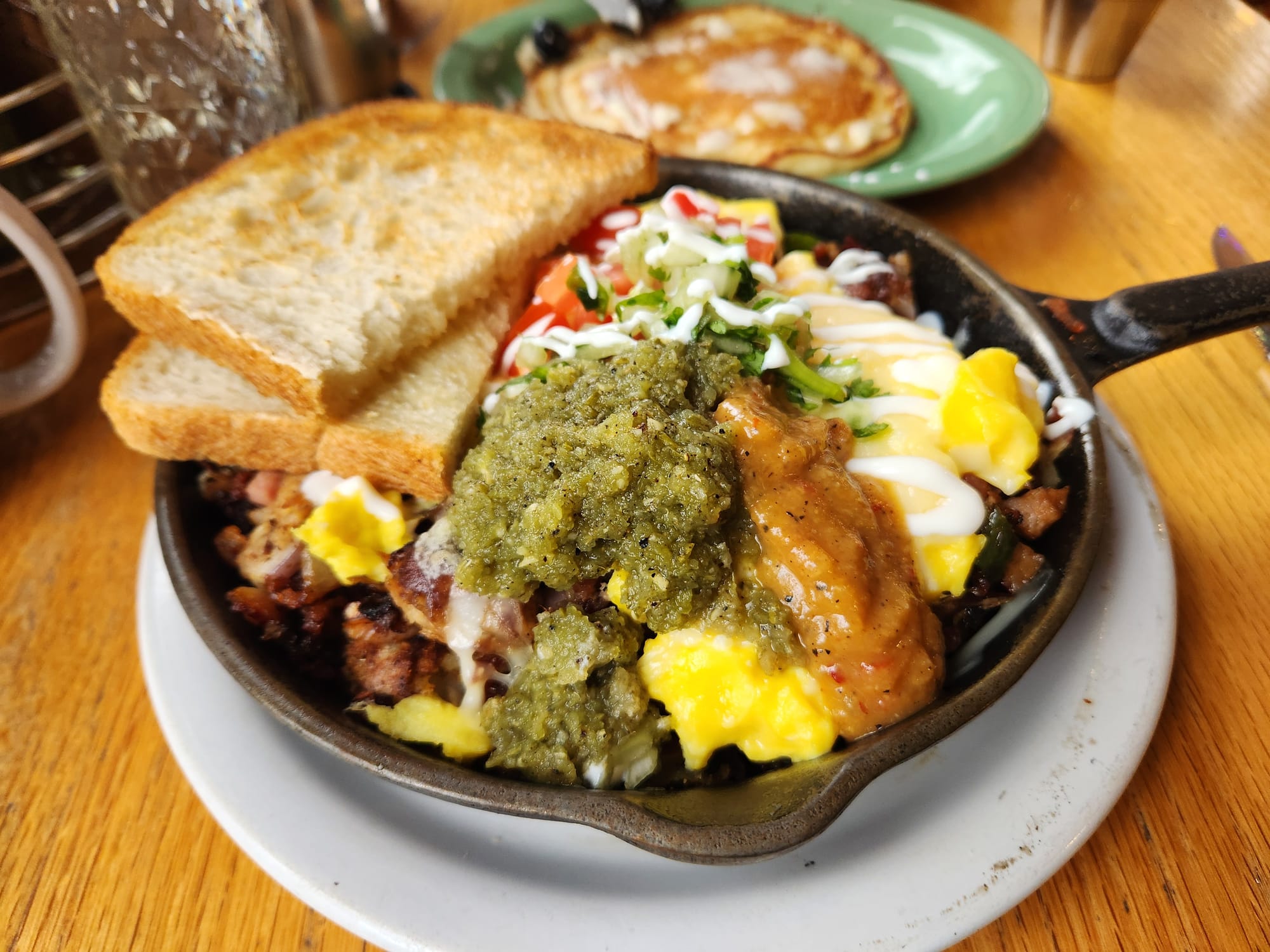 A breakfast skillet, with eggs, hot sauce, toast, and a pancake.