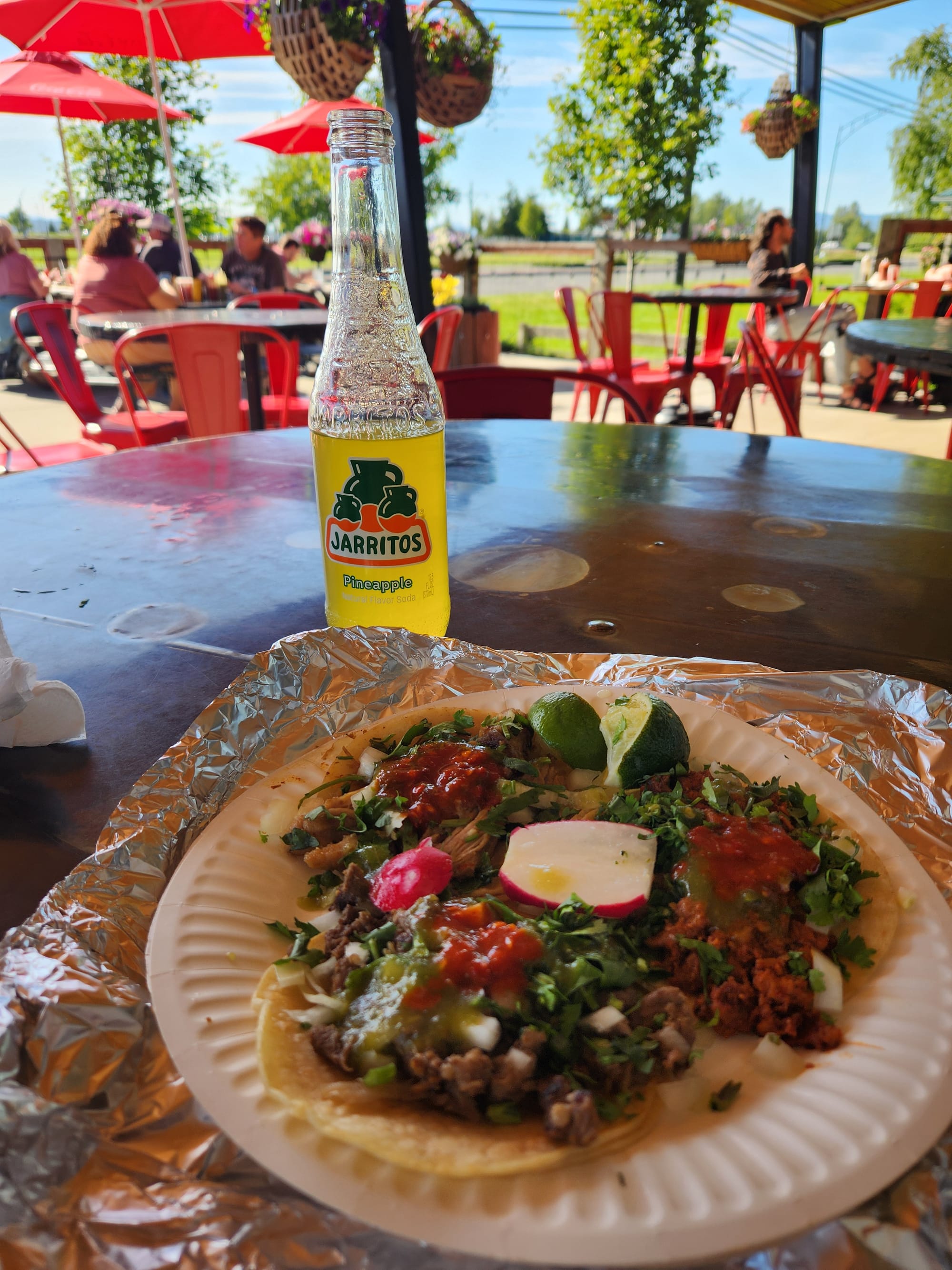 A plate of three tacos with an outdoor covered patio with some people in the background.