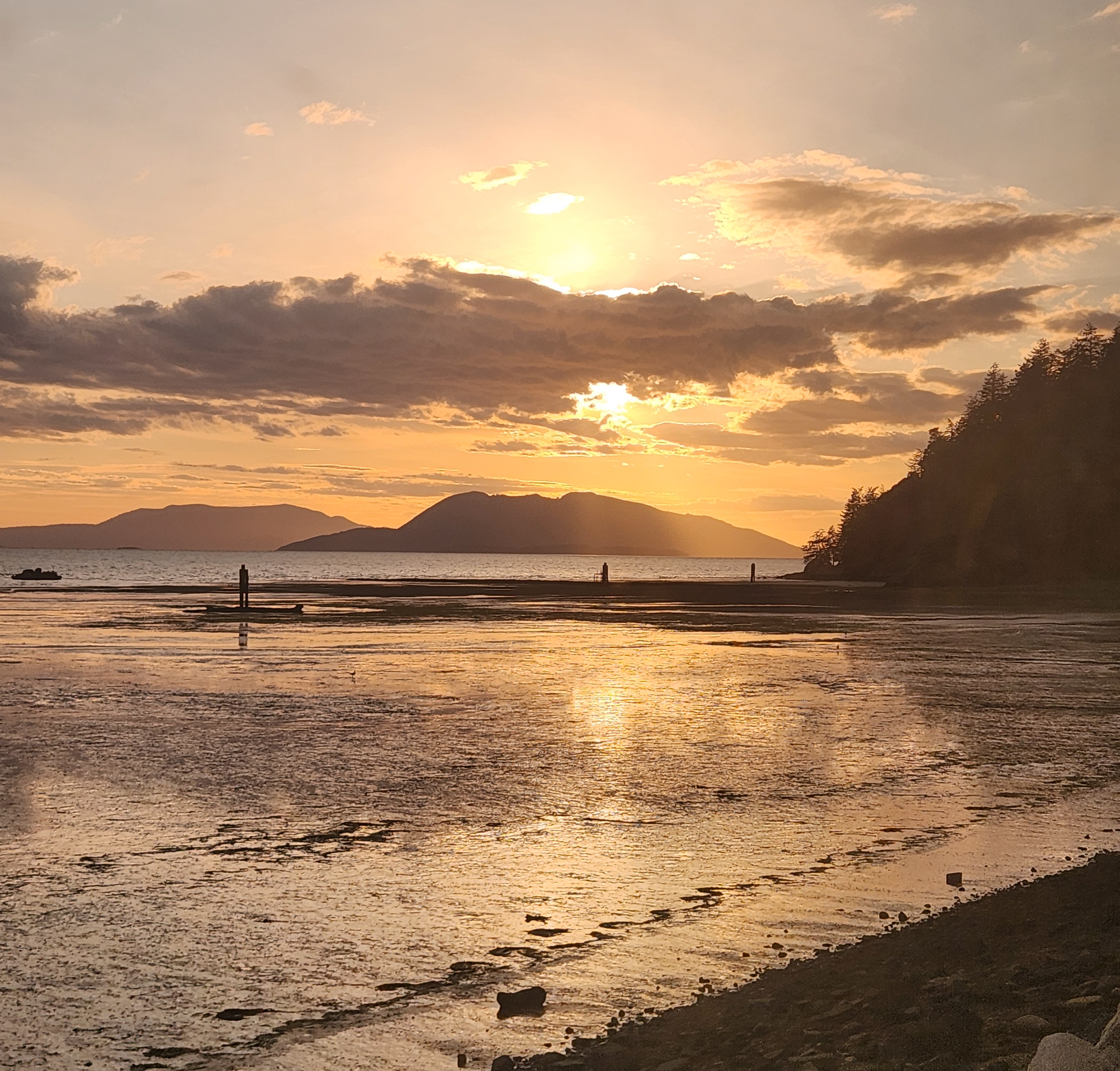 A partly cloudy sunset with the sun reflecting off the tidal mud flats. 