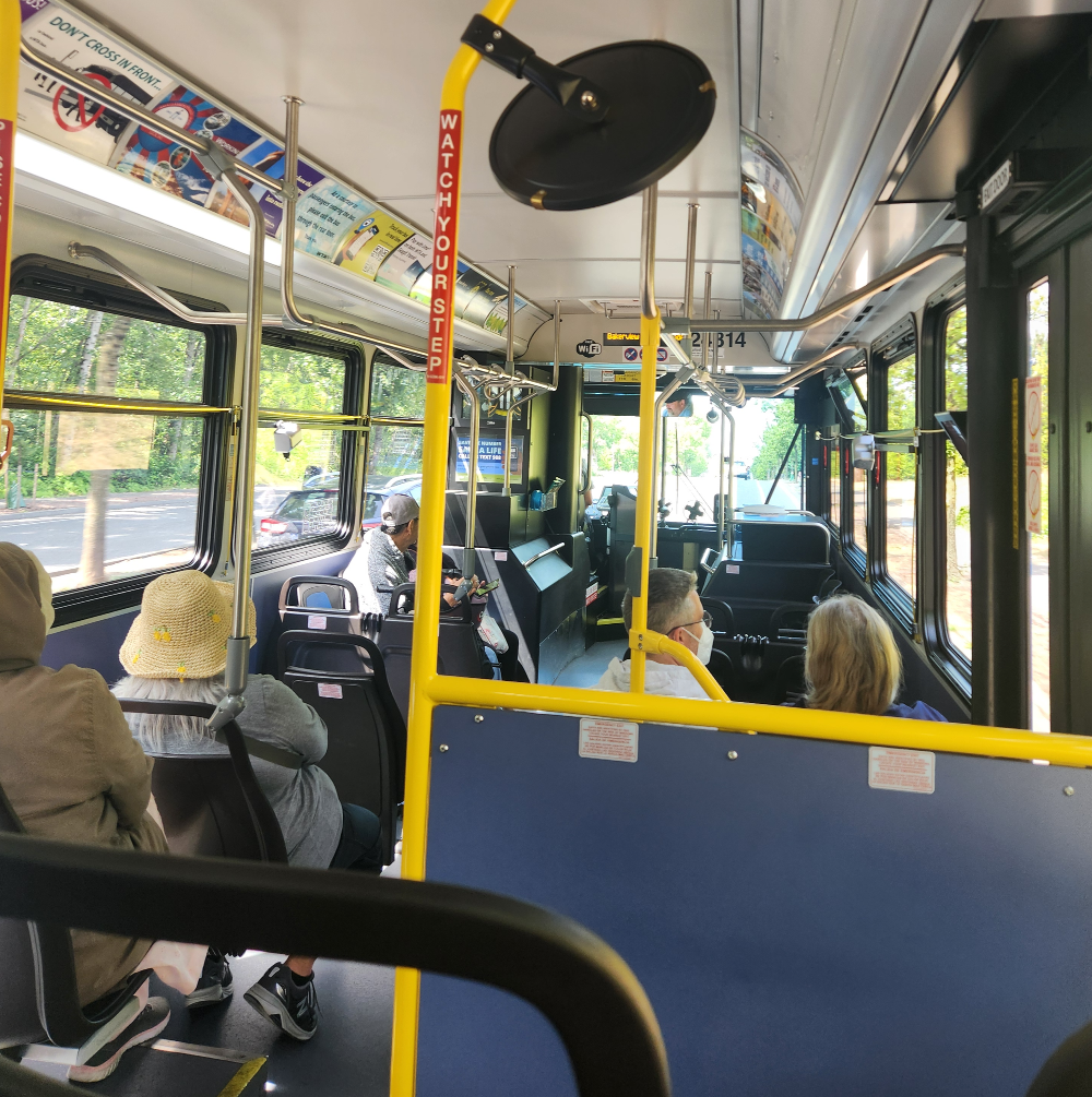 A small handful of passengers sit aboard a bus traveling along an arterial roadway.