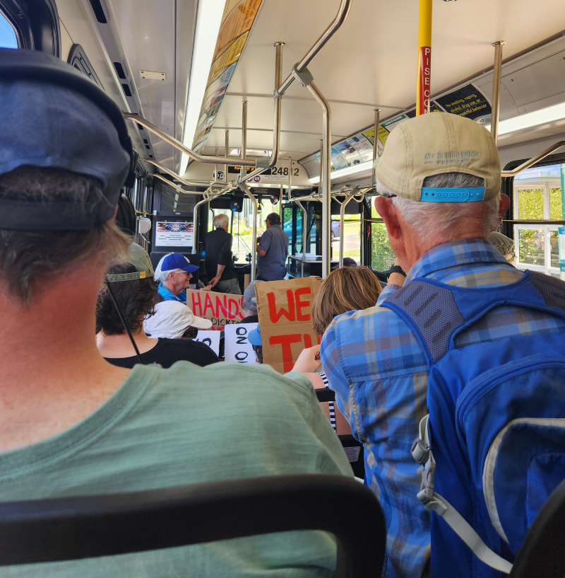 An interior of a packed bus, with people carrying protest signs.