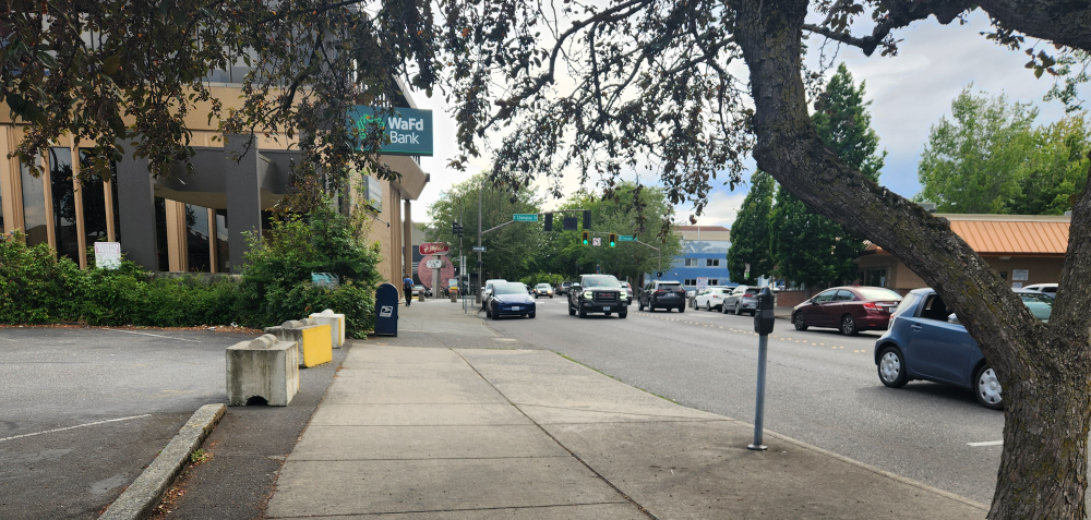 A sidewalk along a street with vehicles, with a WaFd Bank building at the left.