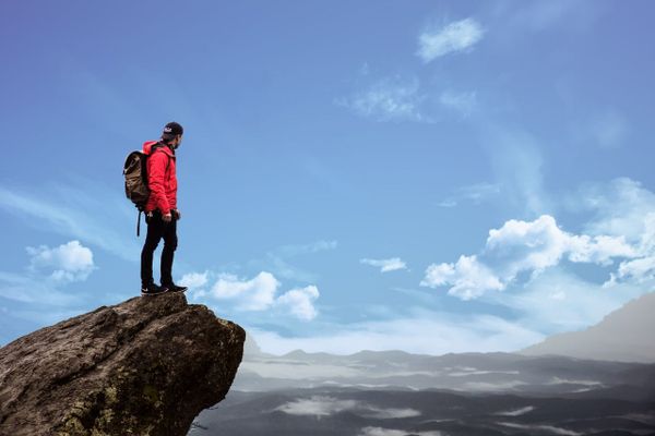 Man in red jacket stood on cliff top overlooking the landscape of possibilities. 