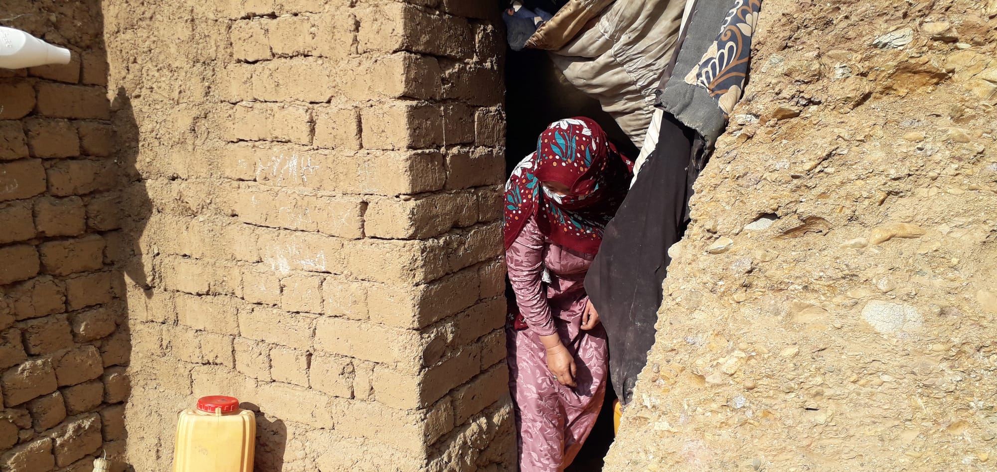 Jagra Khel settlement, Mountain valley, Dugout cave home, Mud bricks, Plastic sheets, Metal stove, Embroidery work, Washing dishes, Mixing flour, Preparing bread, Cleaning, Children, Rugs and carpets, Kettles, bowls, containers, Dari, Bamyan, Afghanistan