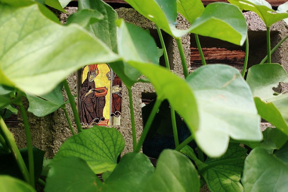 A photo collage of an illustration of Hildegard von Bingen receiving a vision, edited to appear hidden by leaves.